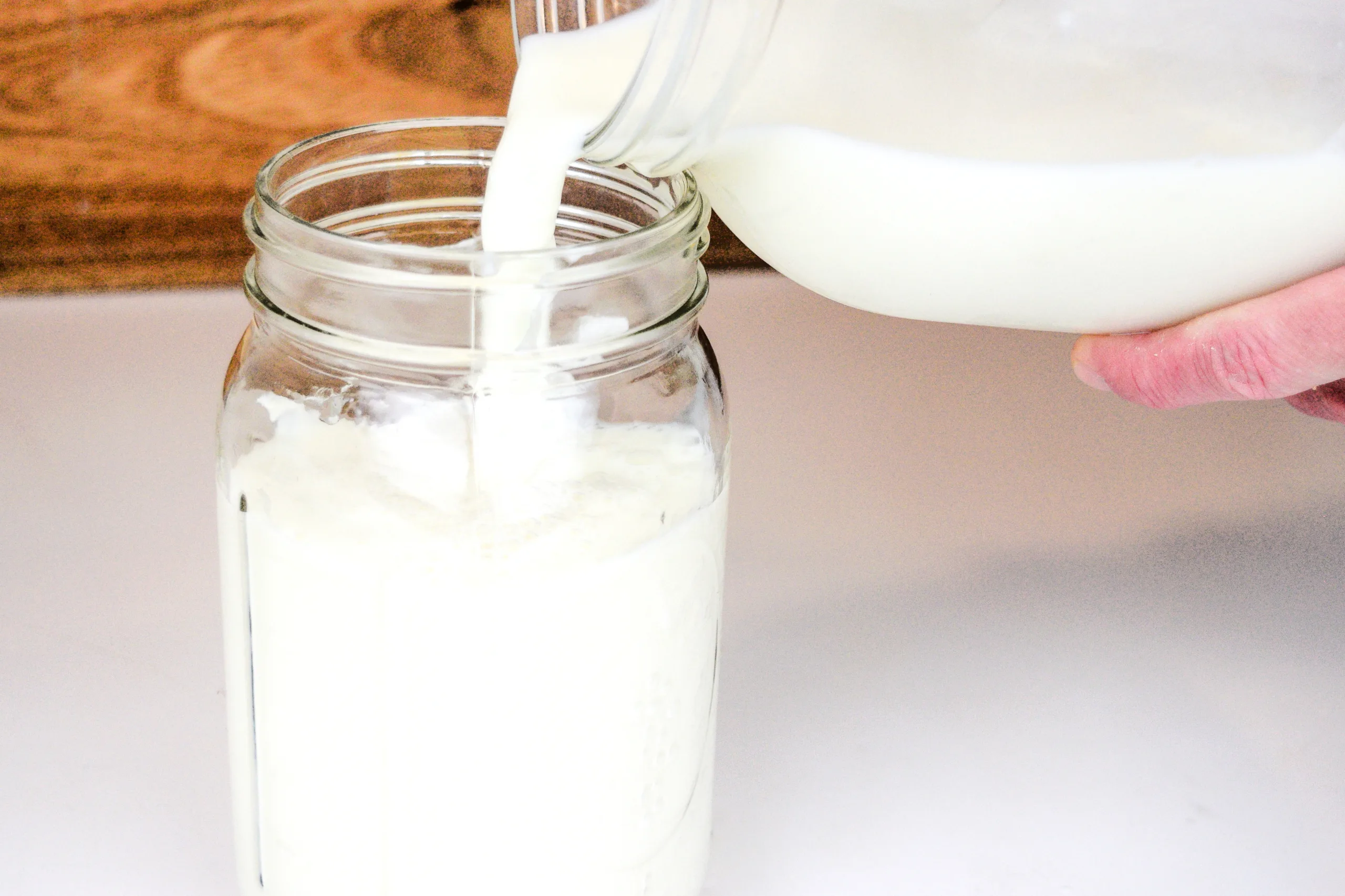 Fresh raw milk being poured into a mason jar to start homemade clabber.