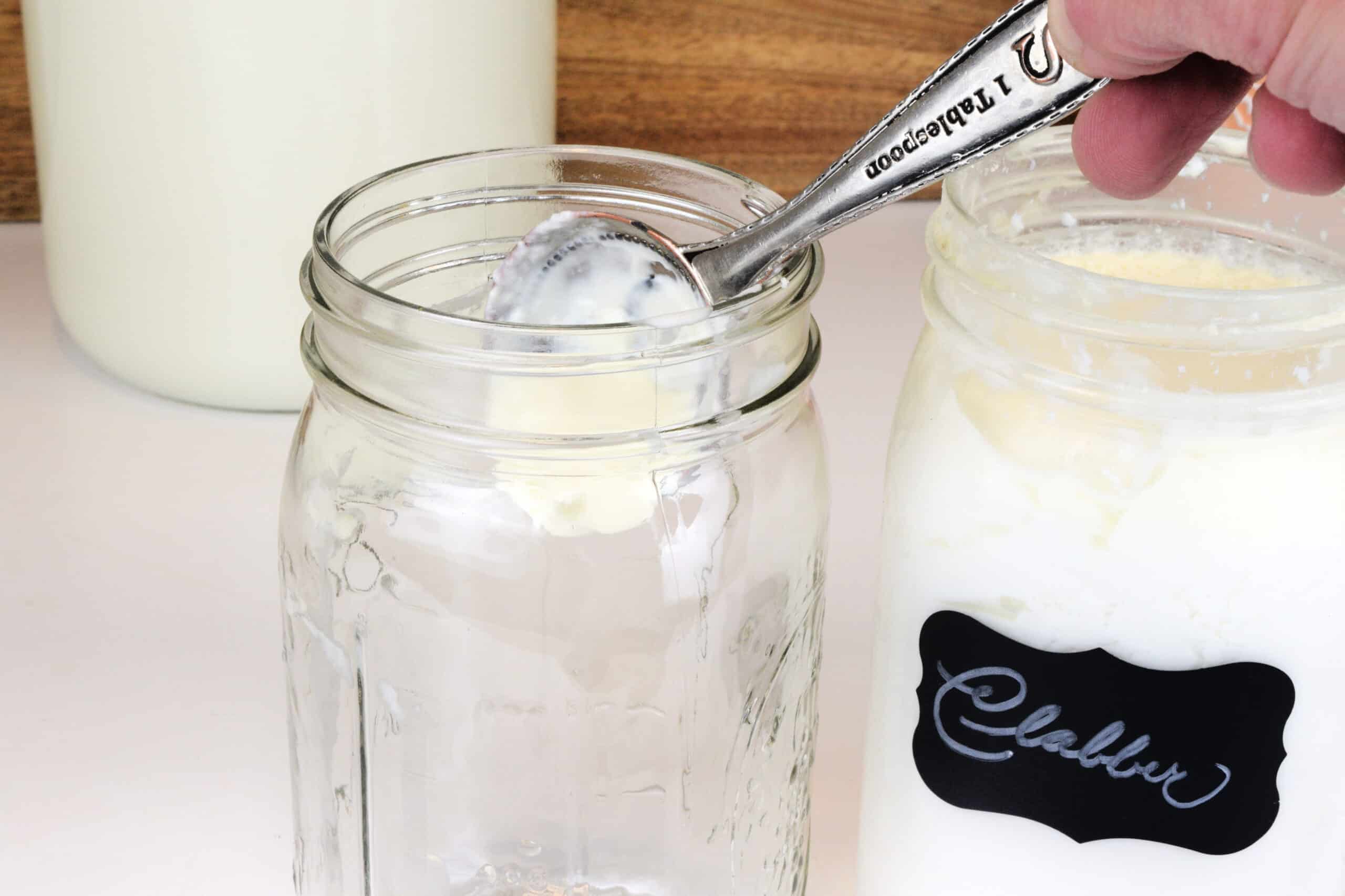 Spoonful of homemade clabber being added to a clean jar to start the next batch.