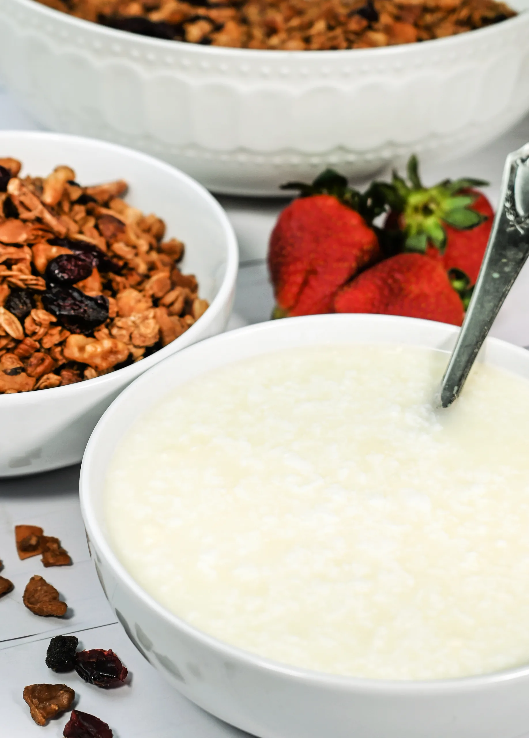 Bowl of homemade raw milk clabber served with granola, strawberries, and a spoon for breakfast.