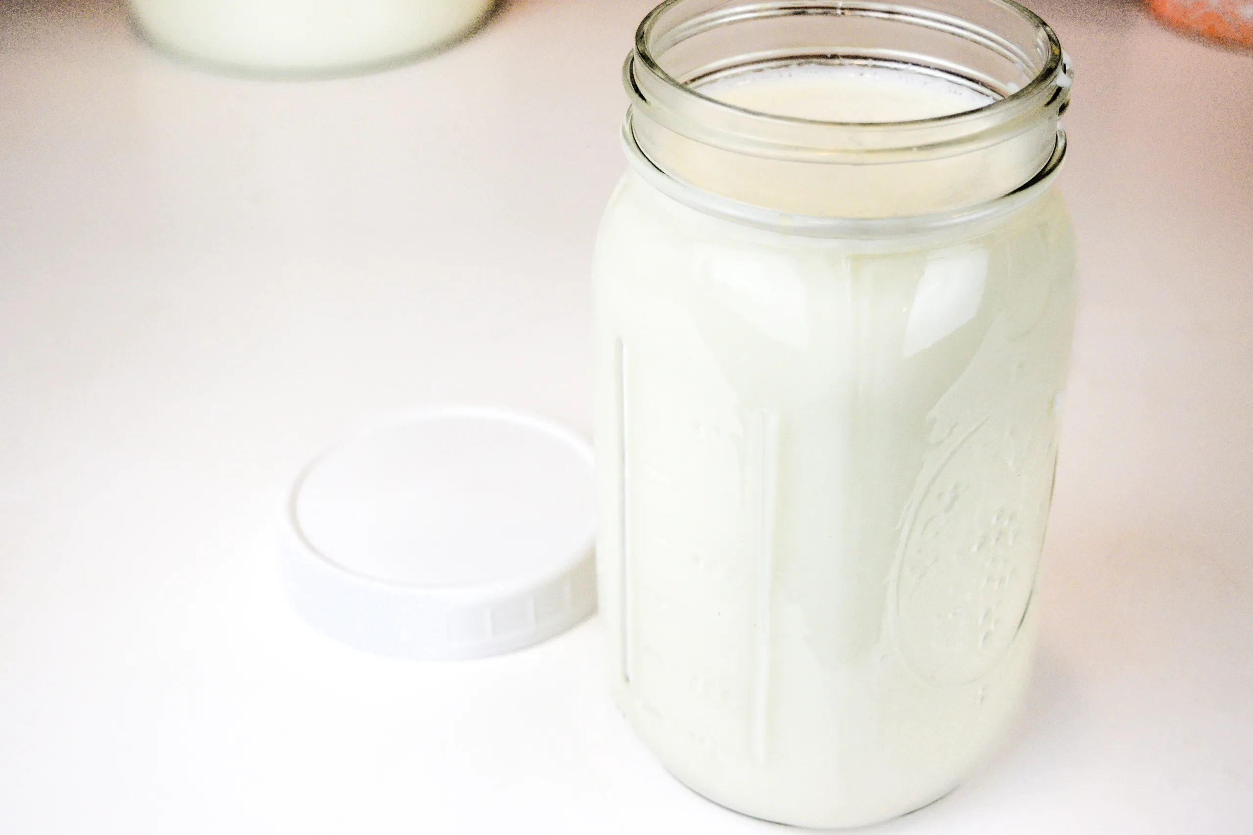 A quart sized jar of raw milk fermenting into clabber on a white table.