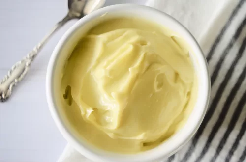 Keto mayonnaise recipe in a white bowl on a white countertop next to a spoon.