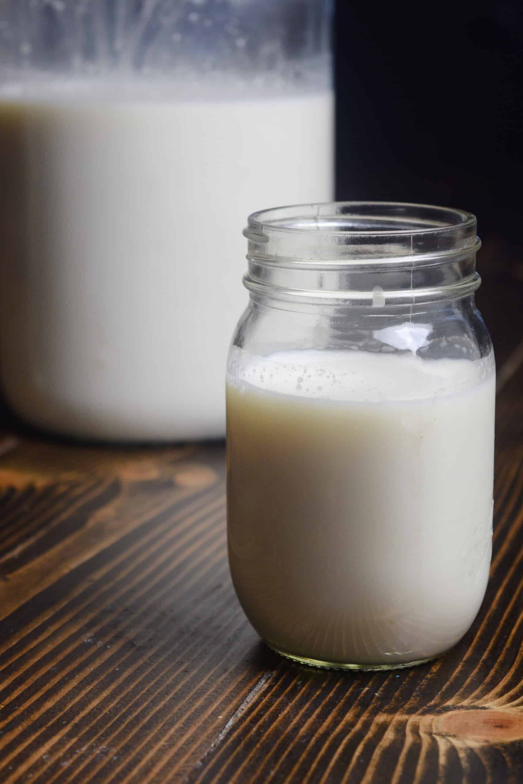 Picture for 13 health benefits of raw dairy consumptions. A mason jar filled with raw dairy milk on a brown table next to a gallon of milk.