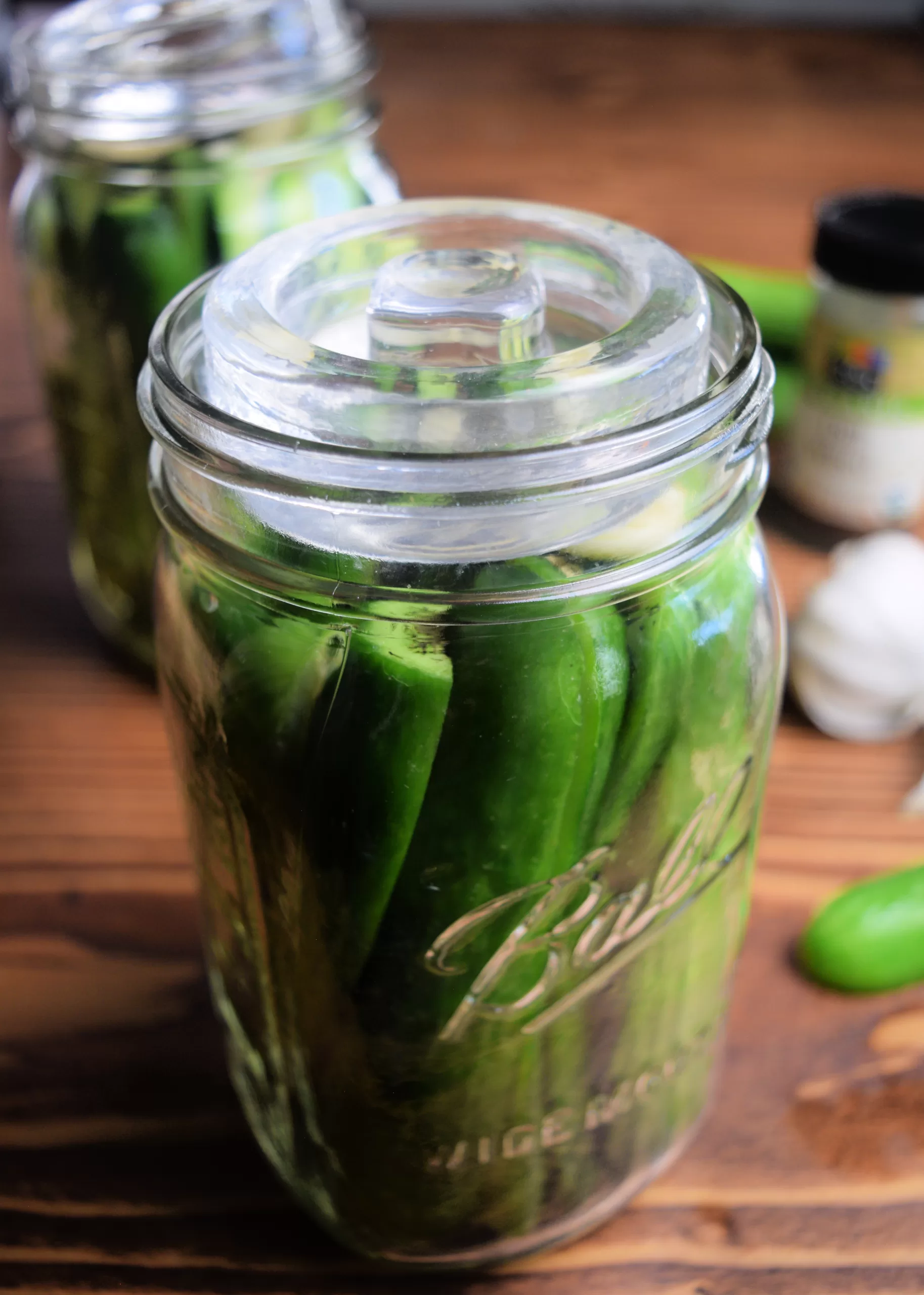 Sliced fermented pickles with garlic and dill in a mason jar next to cucumbers and garlic with a fermentation weight and green burping lid.