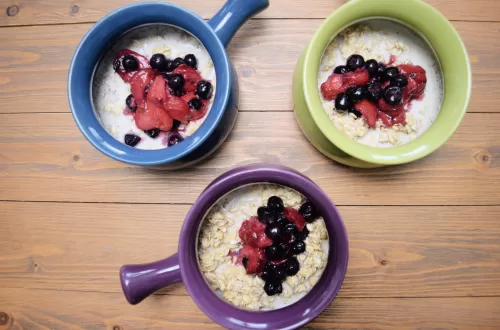 Quick and Easy Quaker Overnight Oats Recipe With Berries - A purple bowl, a green bowl, a blue bowl. filled with overnight oats a mixed berries on a brown tabletop.