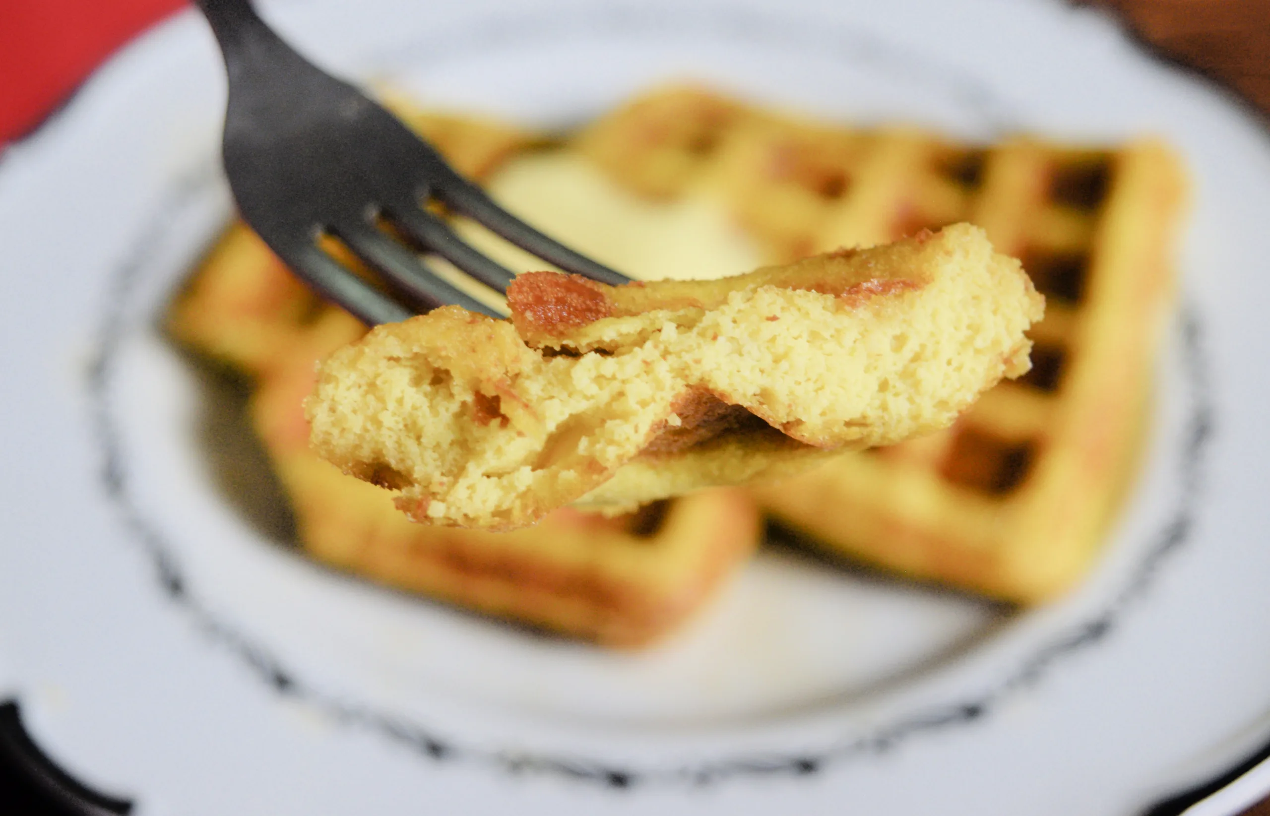 A fork holding piece of Gluten Free waffle with a bit taken out of it.