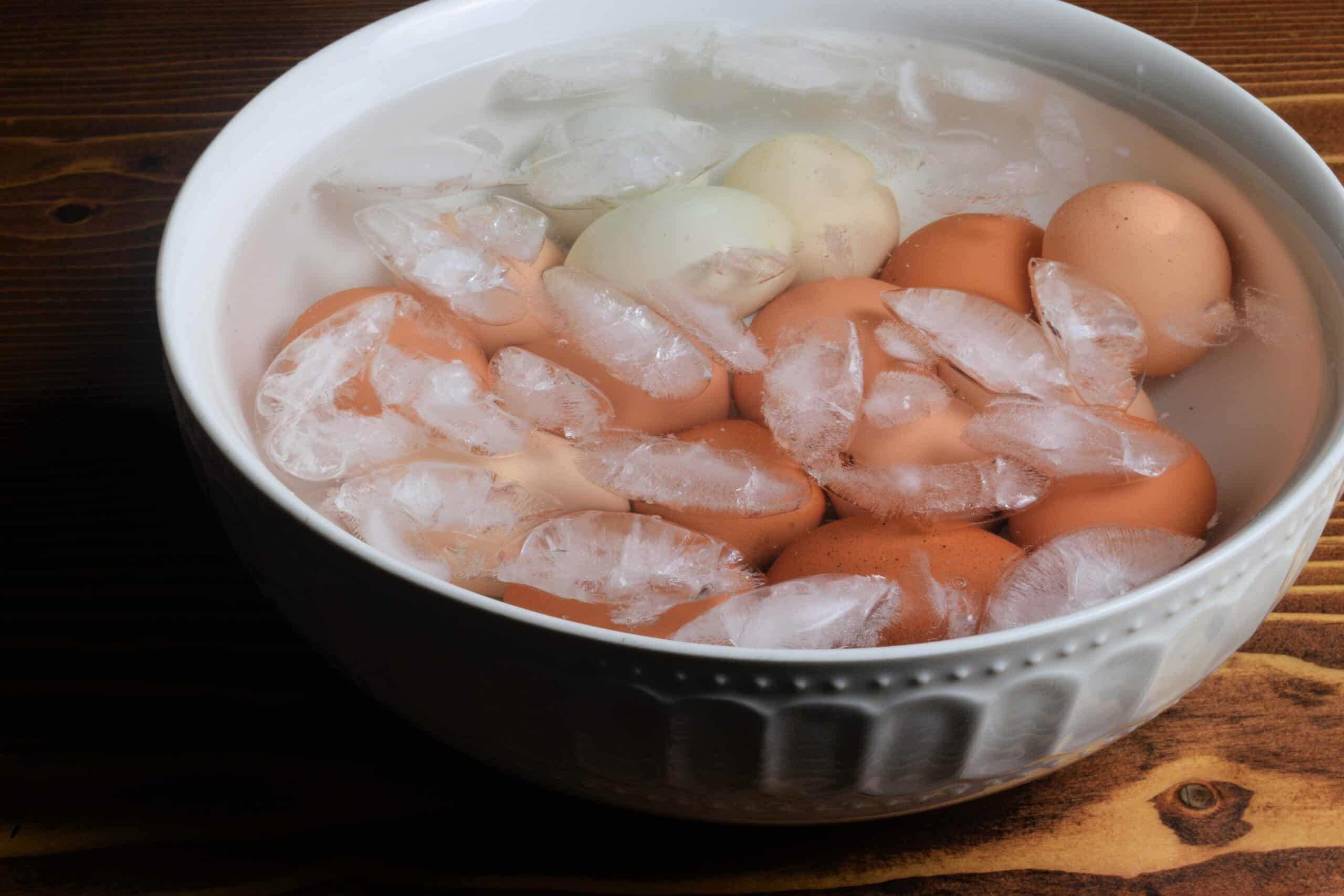 Hard boiled eggs in a white bowl covered with water and ice.