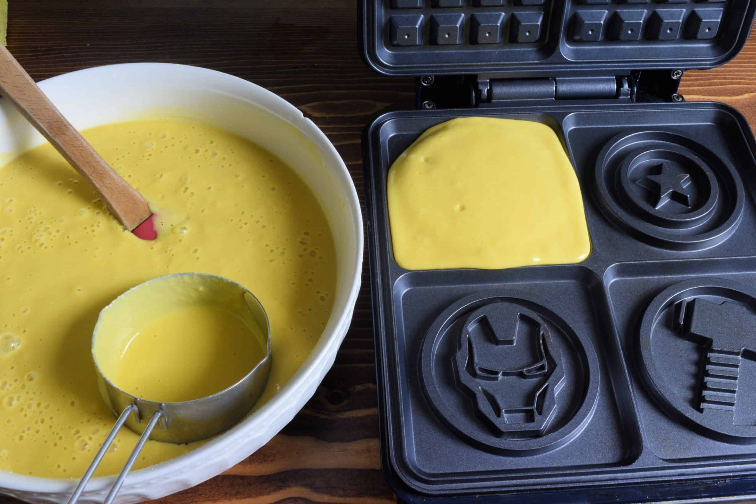 Gluten free waffle batter in a white bowl next to a black waffle iron with the Avengers printed on it.