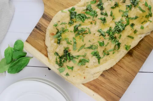 Easy italian sourdough flatbread discard recipe on a pizza stone, with fresh basil on the side and white plates next to it on a white countertop.