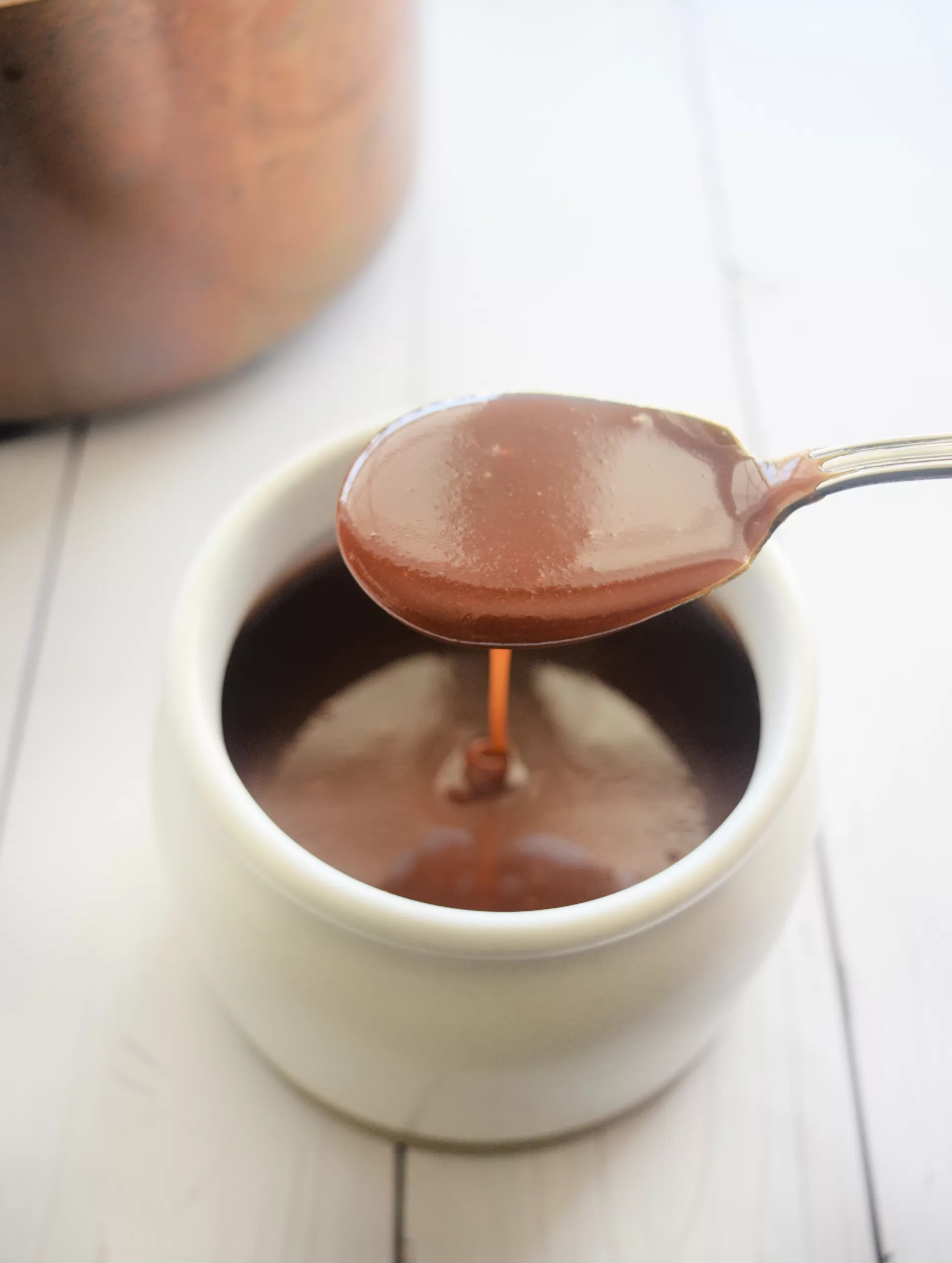 Spoon lifting glossy homemade soft caramel sauce from a jar to show the smooth texture.