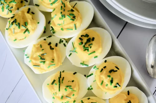 Low carb deviled eggs, three deviled eggs with chives on a white plate and white countertop.