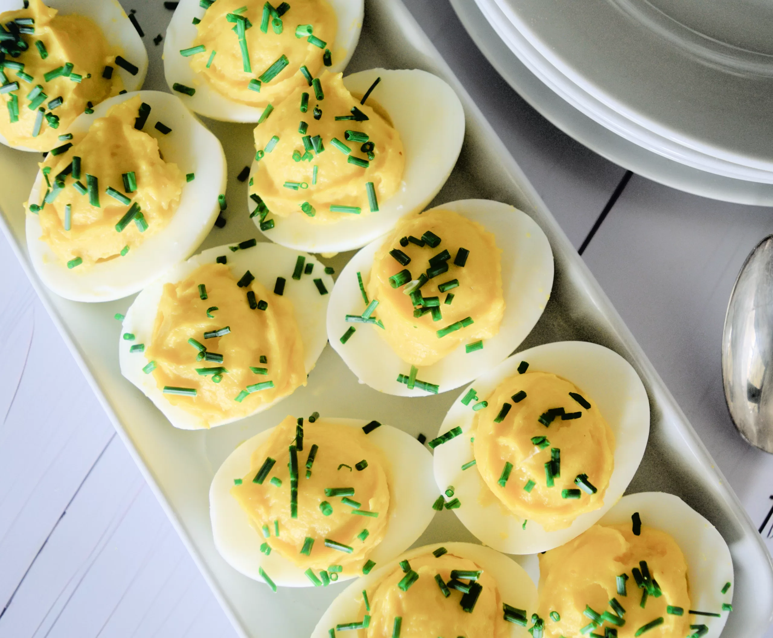 Low carb deviled eggs, three deviled eggs with chives on a white plate and white countertop.