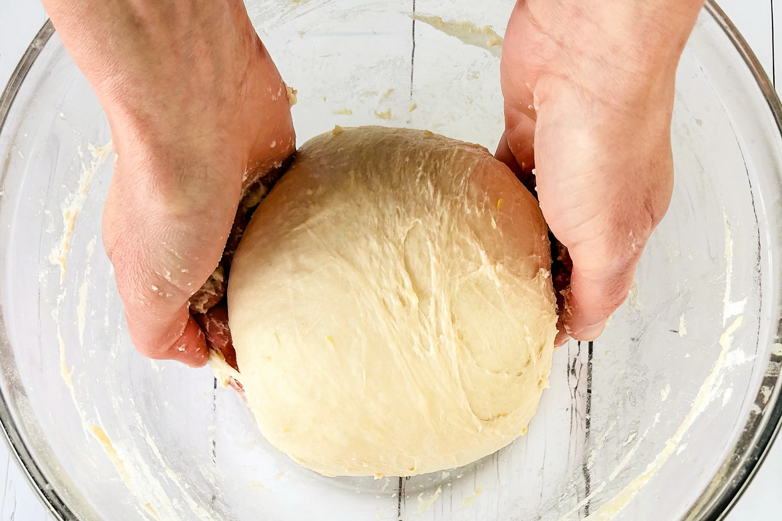 Hands folding and shaping lemon sourdough dough in a glass bowl.