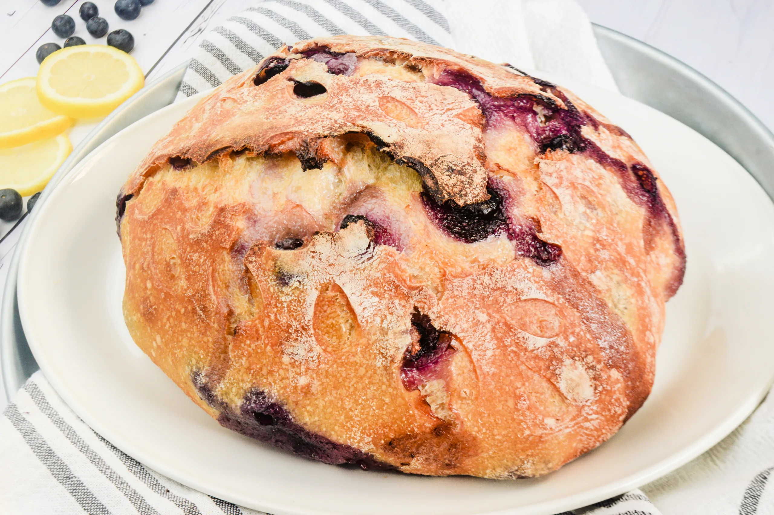 Freshly baked lemon blueberry sweet sourdough bread on a white platter with lemon slices and blueberries.