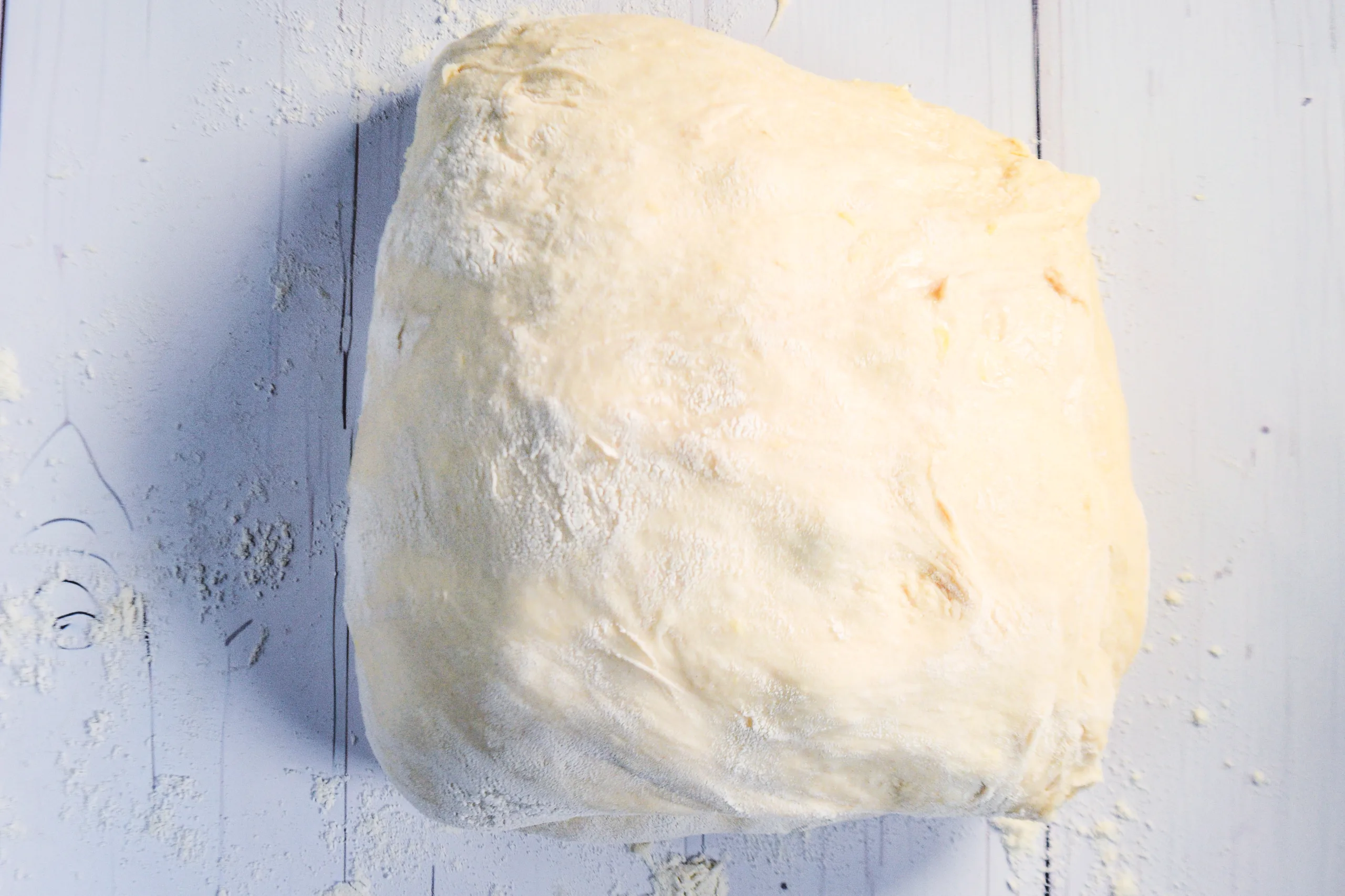 Soft lemon sourdough dough turned out onto a floured surface and shaped with blueberries inside.