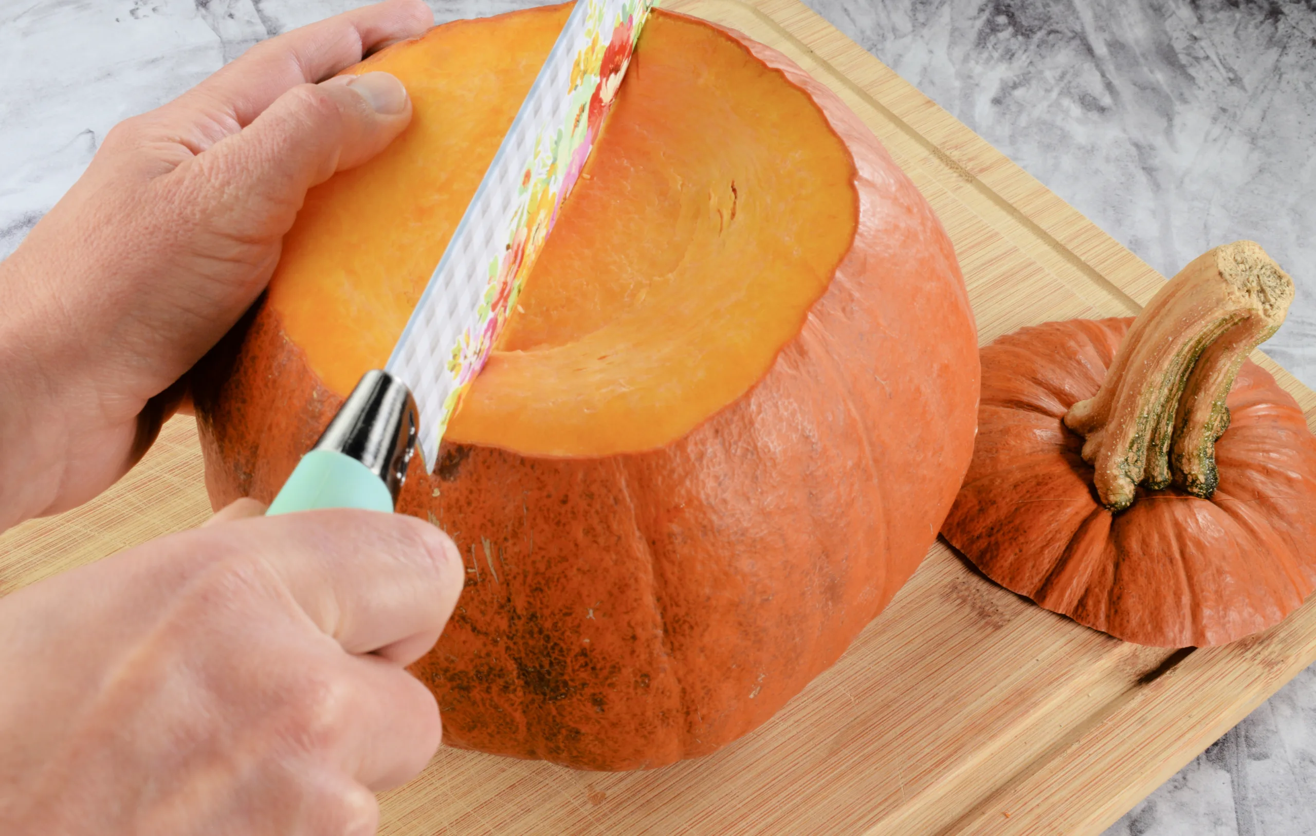 Knife cutting through a pumpkin on a wooden cutting board.
