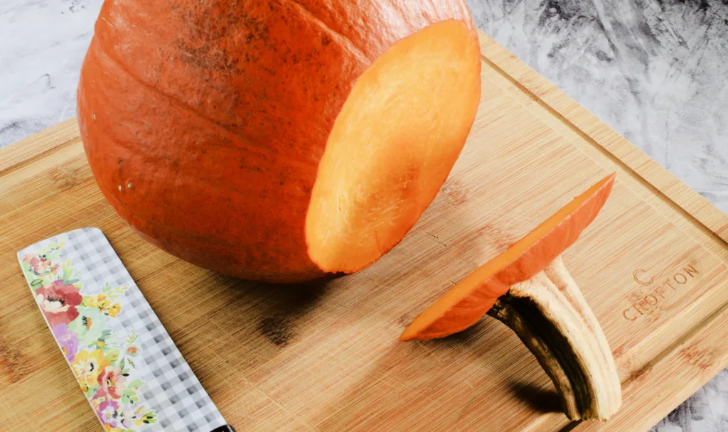 Whole pumpkin being cut for How to Roast a Whole Pumpkin to Make Pumpkin Purée.