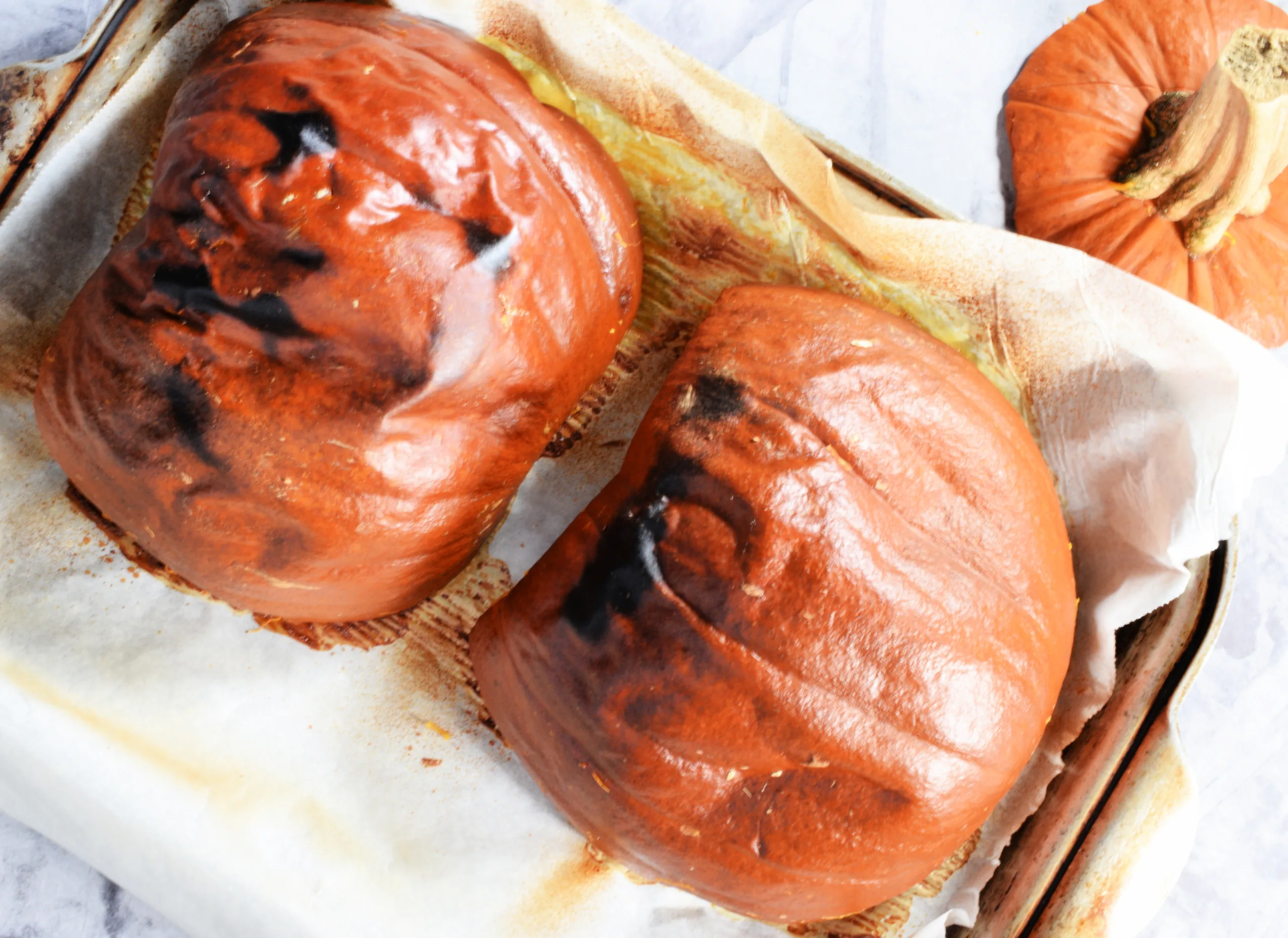 Roasted pumpkin halves on a parchment-lined baking sheet after baking.