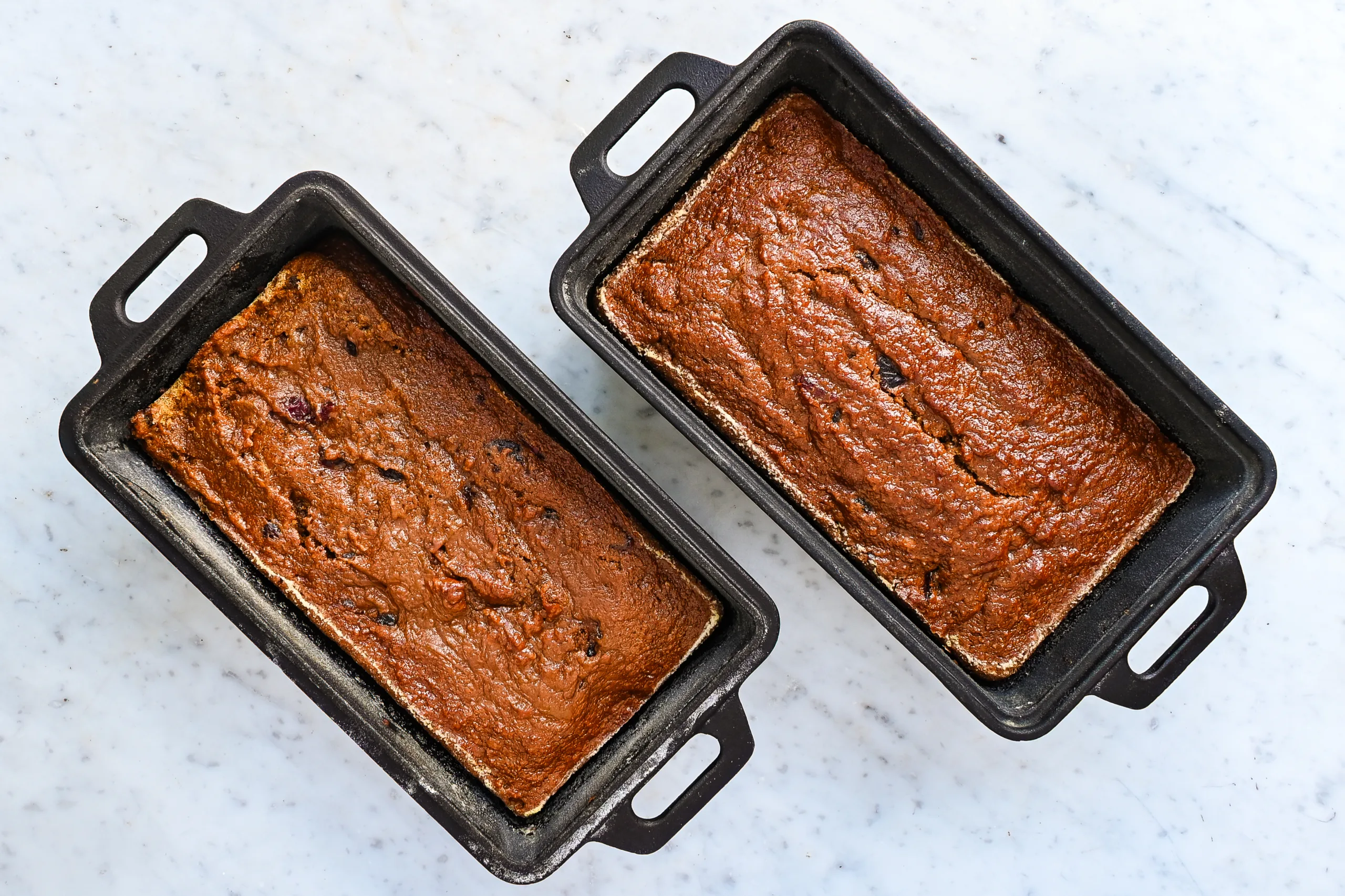 Two baked loaves of sourdough pumpkin cranberry quick bread in loaf pans.
