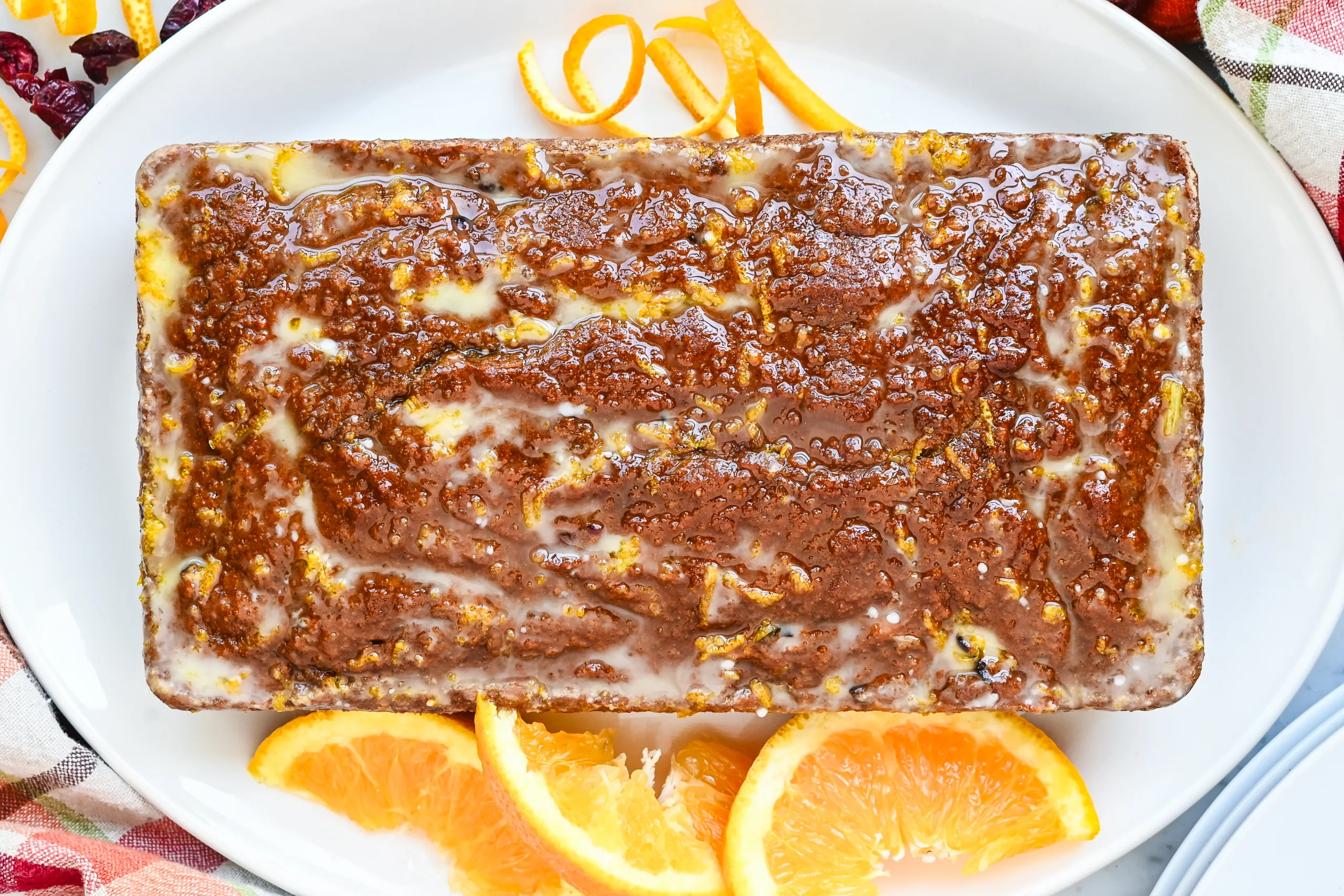 Glazed pumpkin cranberry quick bread loaf with orange slices and orange peel.