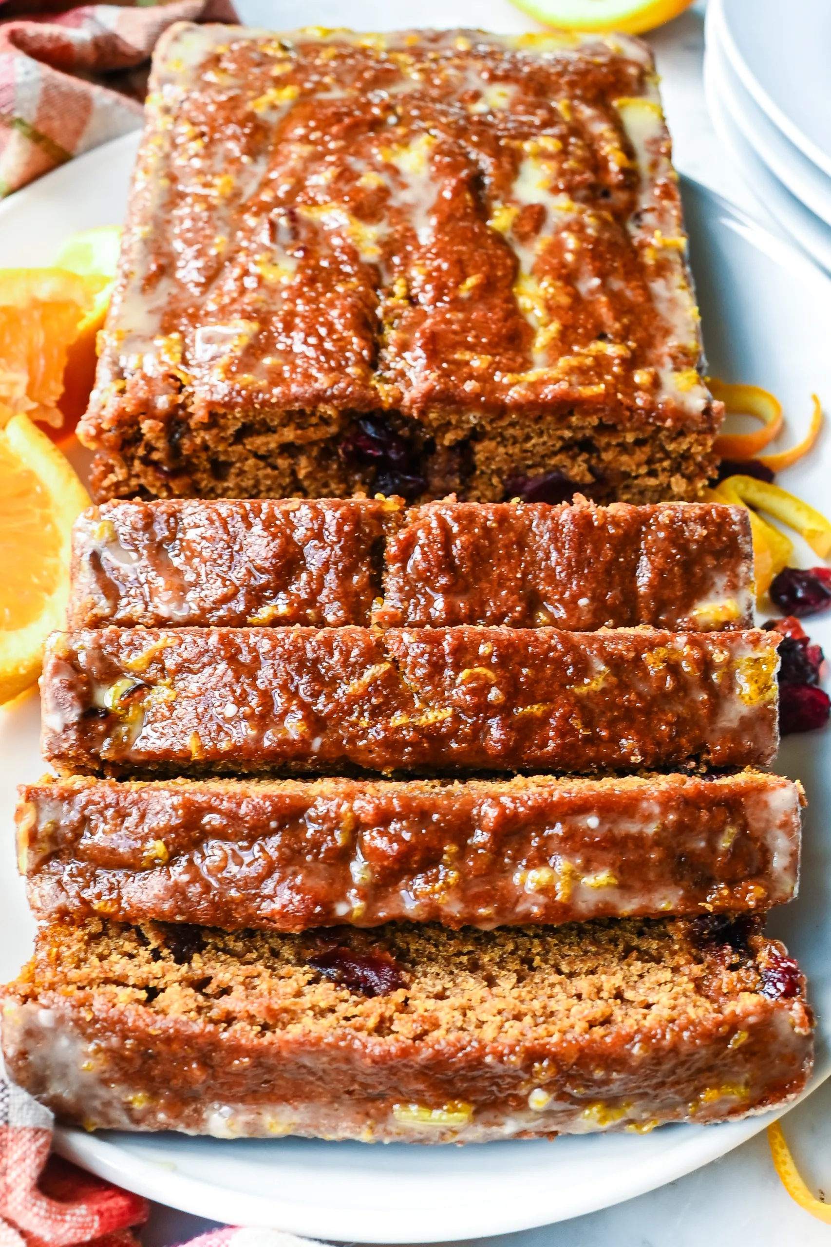 Slices of sourdough pumpkin cranberry quick bread arranged in front of a glazed loaf.