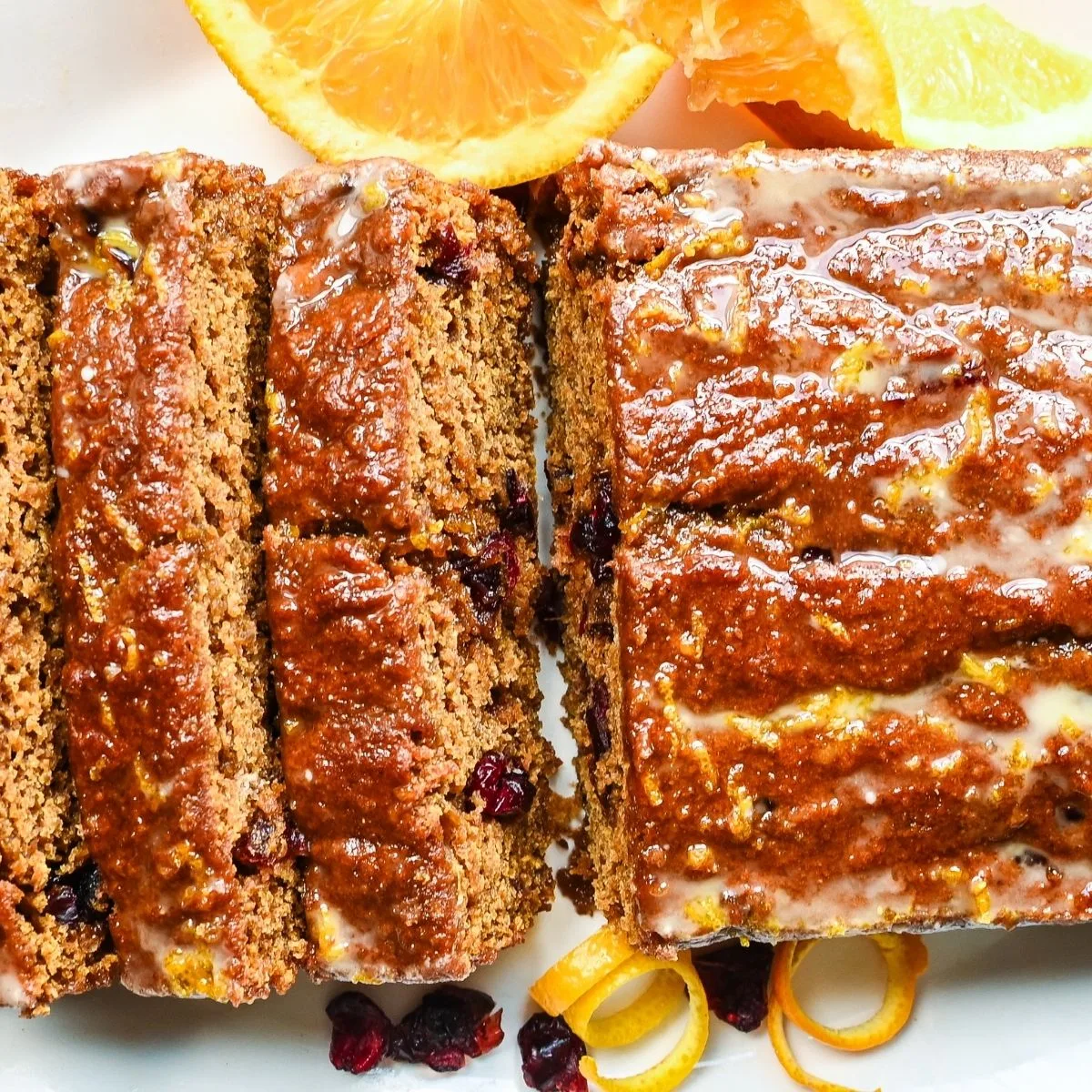 Sliced sourdough pumpkin cranberry quick bread with orange glaze on a white serving platter.