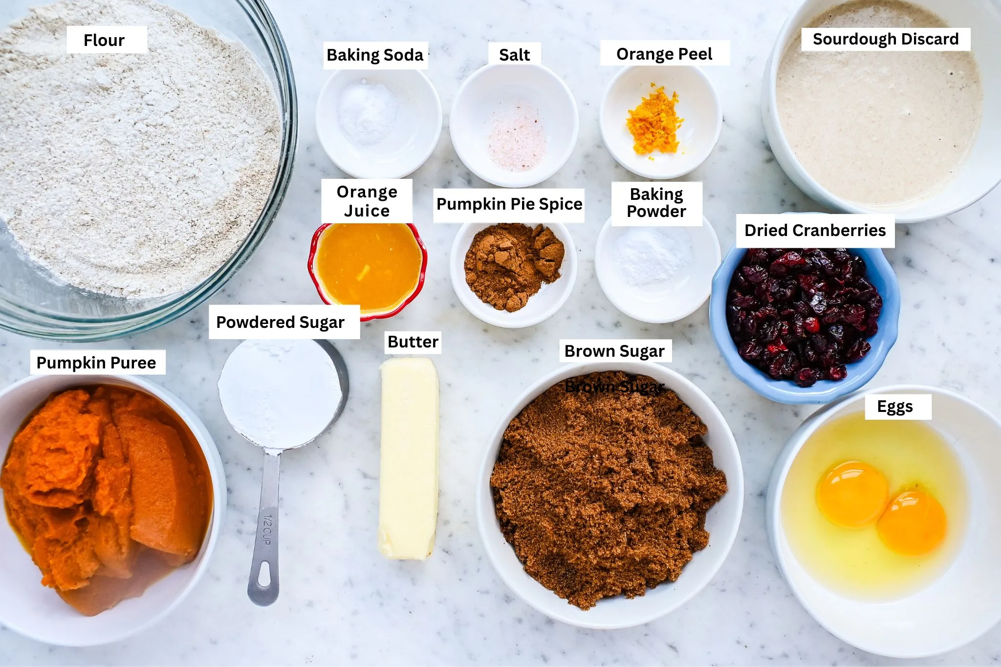 Ingredients for sourdough pumpkin cranberry quick bread arranged on a marble counter.