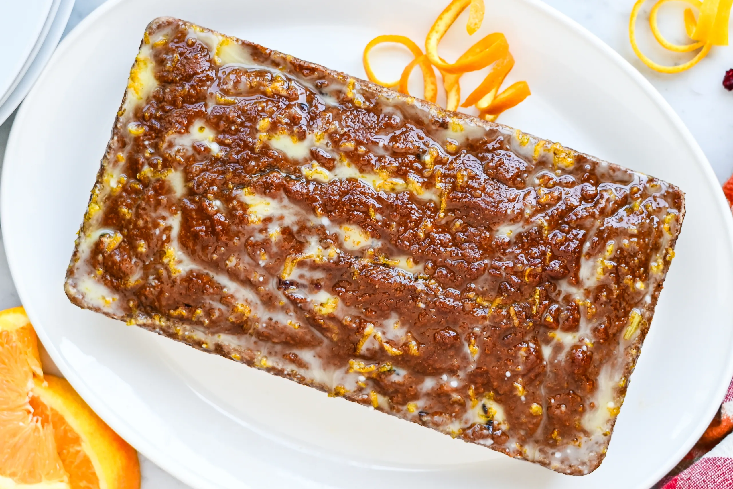 Glazed pumpkin cranberry quick bread loaf with orange slices and orange peel.