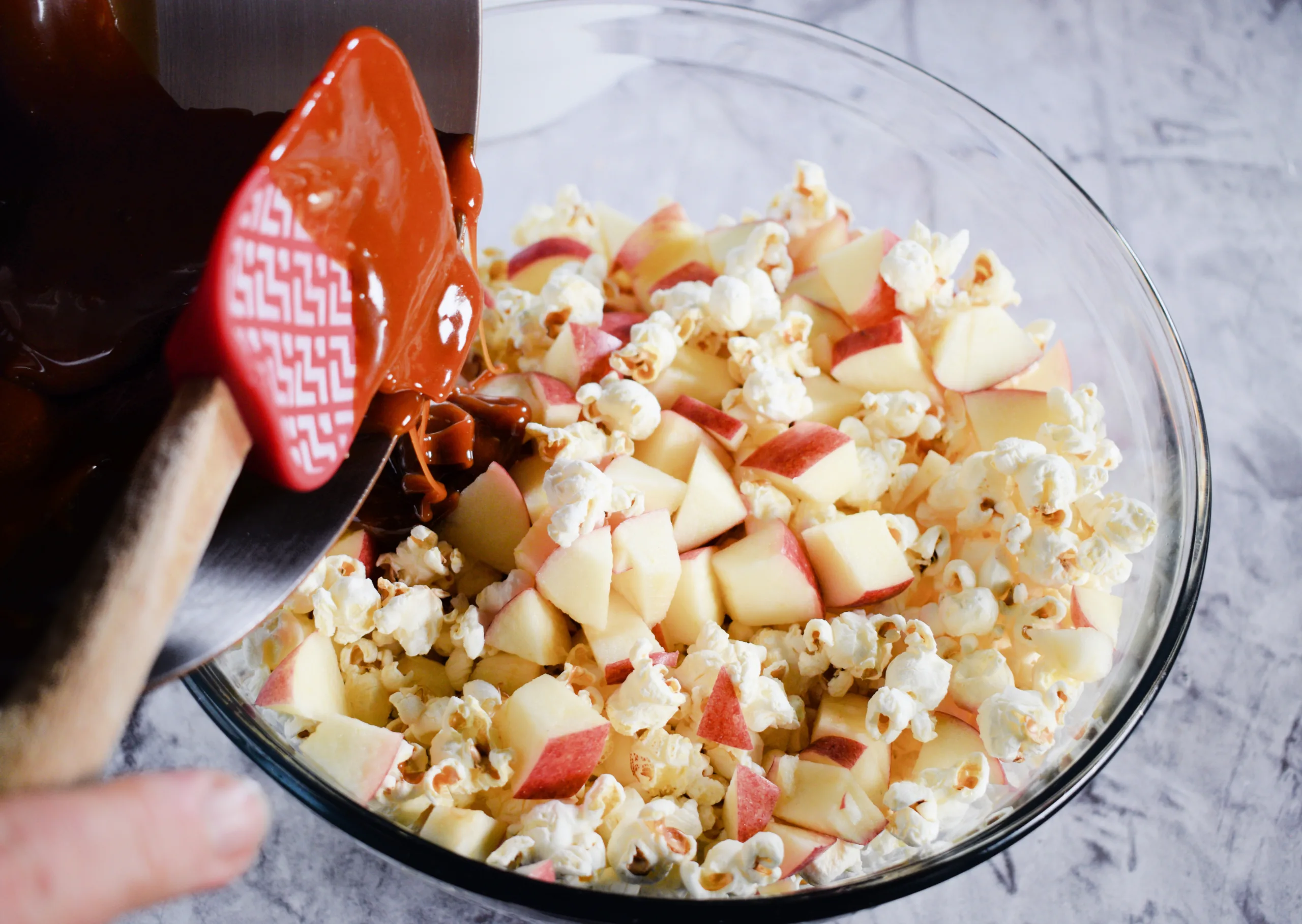 Caramel being poured over a popcorn apple mixture for Homemade Caramel Apple Popcorn Without Corn Syrup.