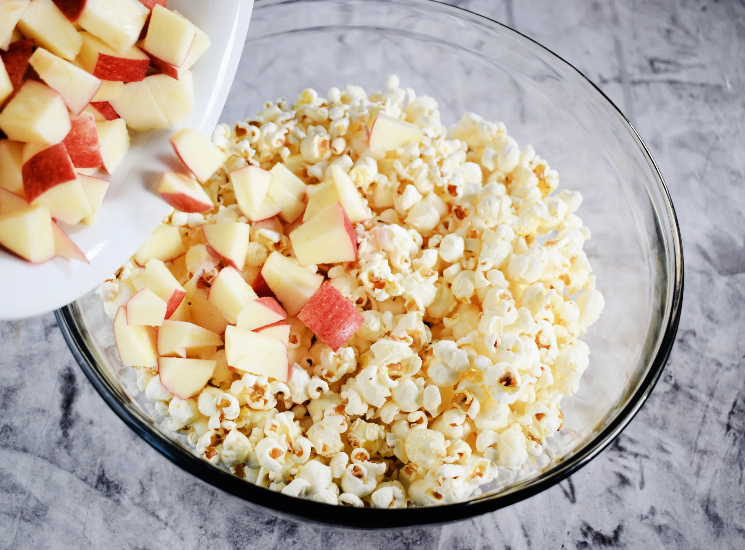 Apples being poured popcorn for Homemade Caramel Apple Popcorn Without Corn Syrup.