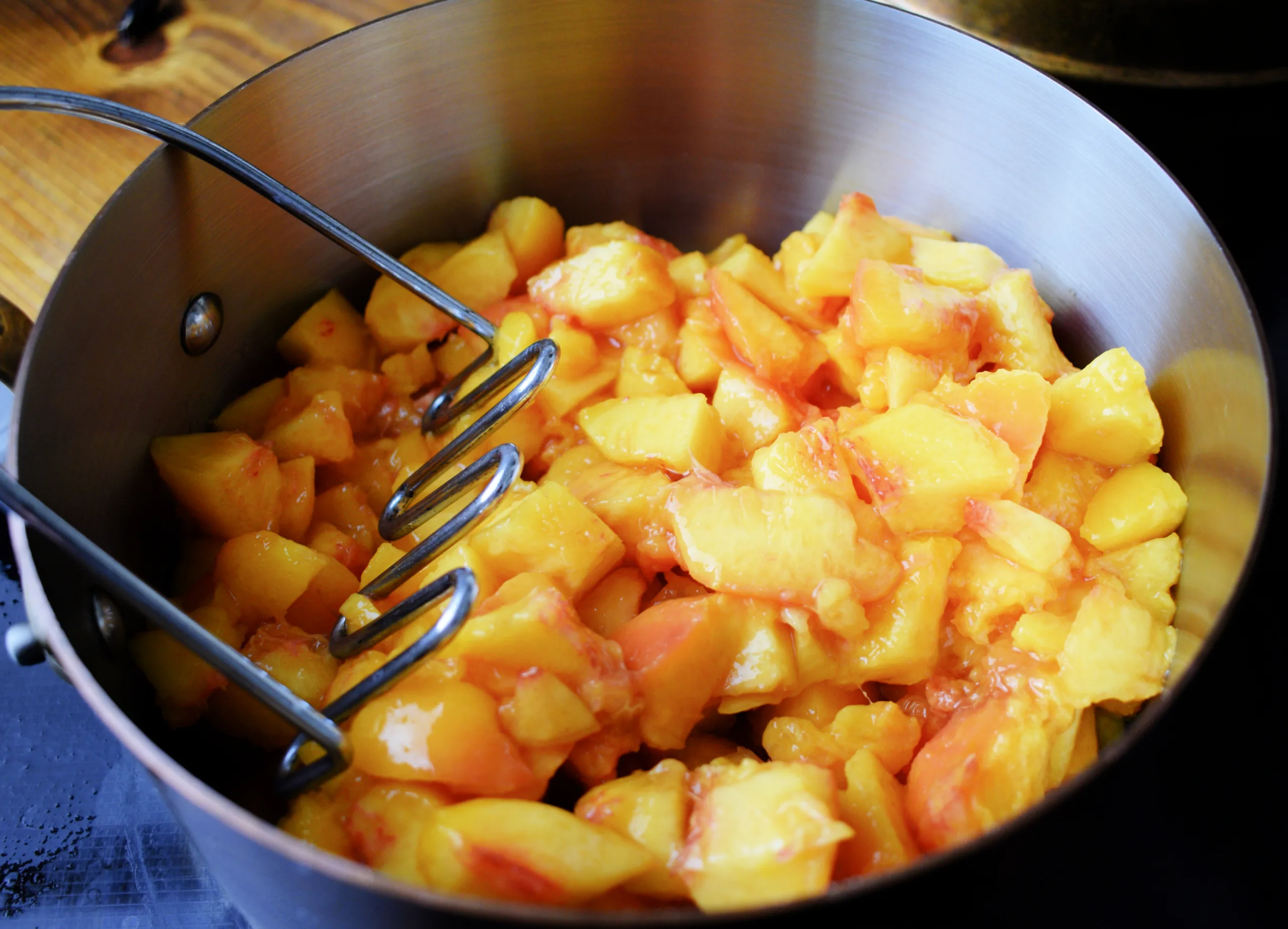 Mashing peaches for Peached being blanched for Low Sugar Peach Jam (Easy Canning Recipe - No Pectin).