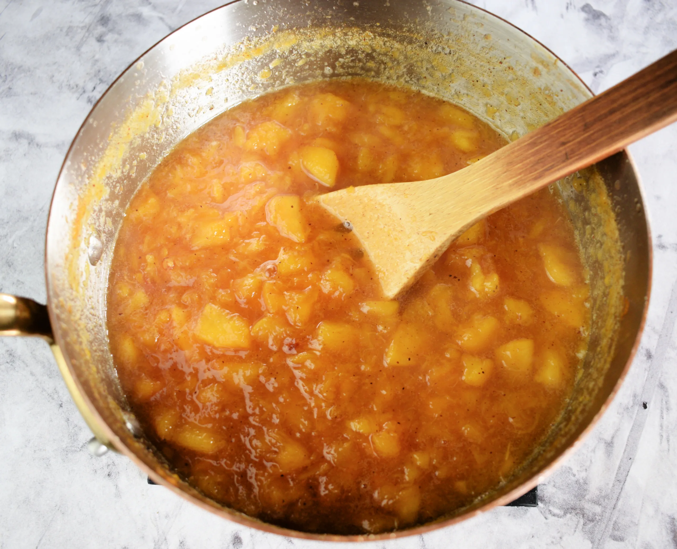 Low sugar peach jam cooking in a pot with a wooden spoon as the peaches thicken.