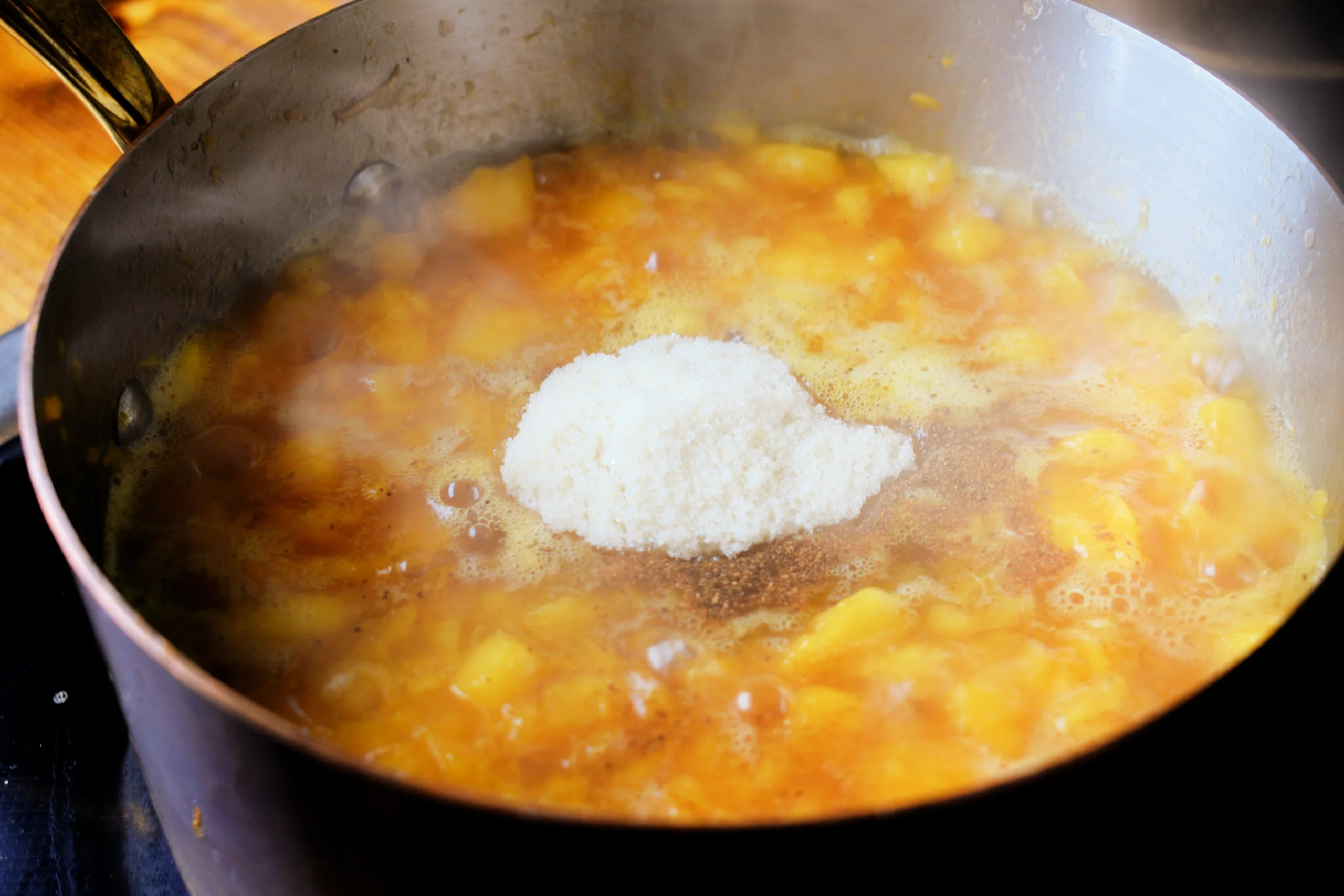 Sugar and cinnamon added to simmering chopped peaches in a pot.