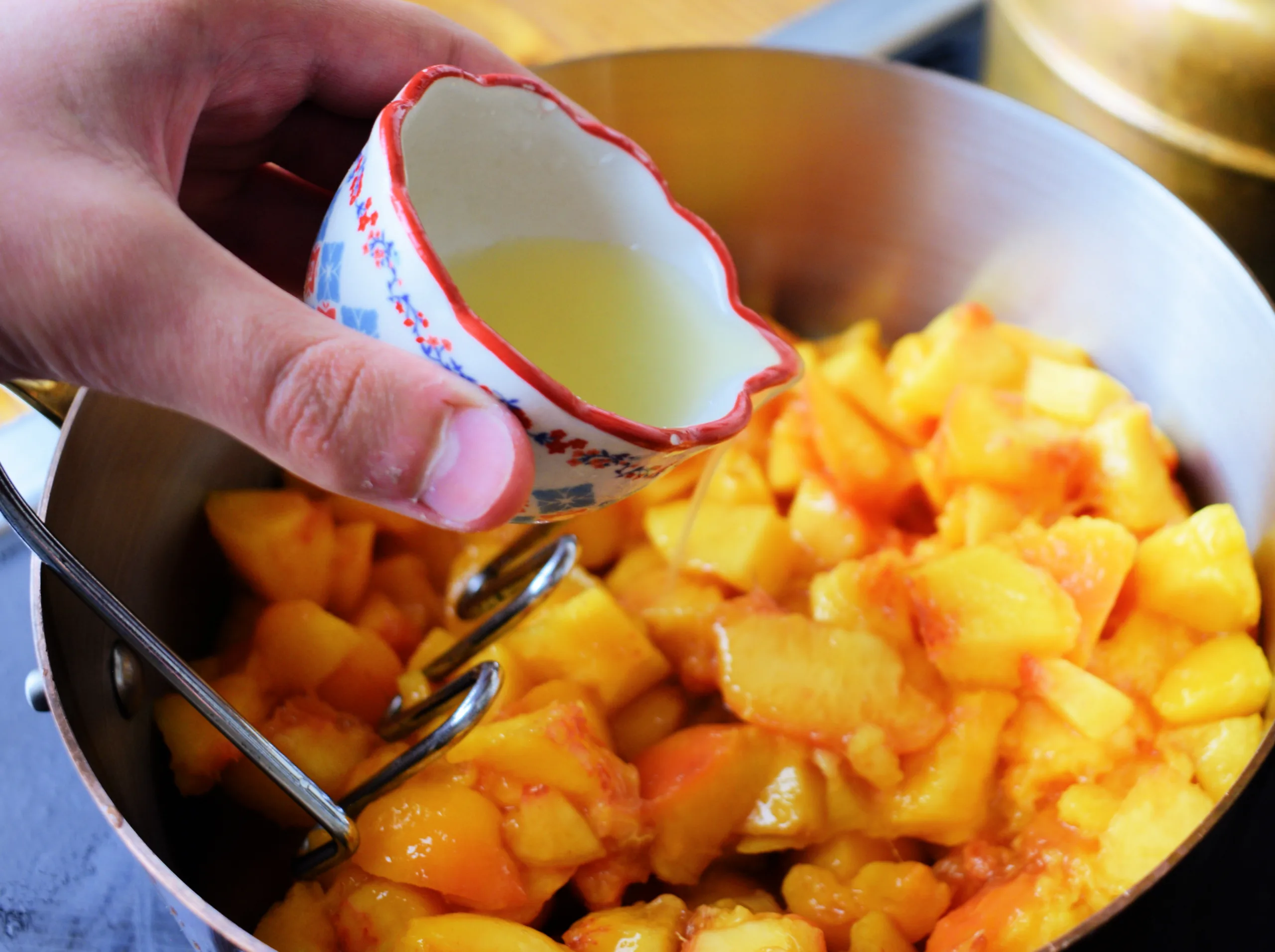Lemon juice being poured over chopped peaches before making peach jam.