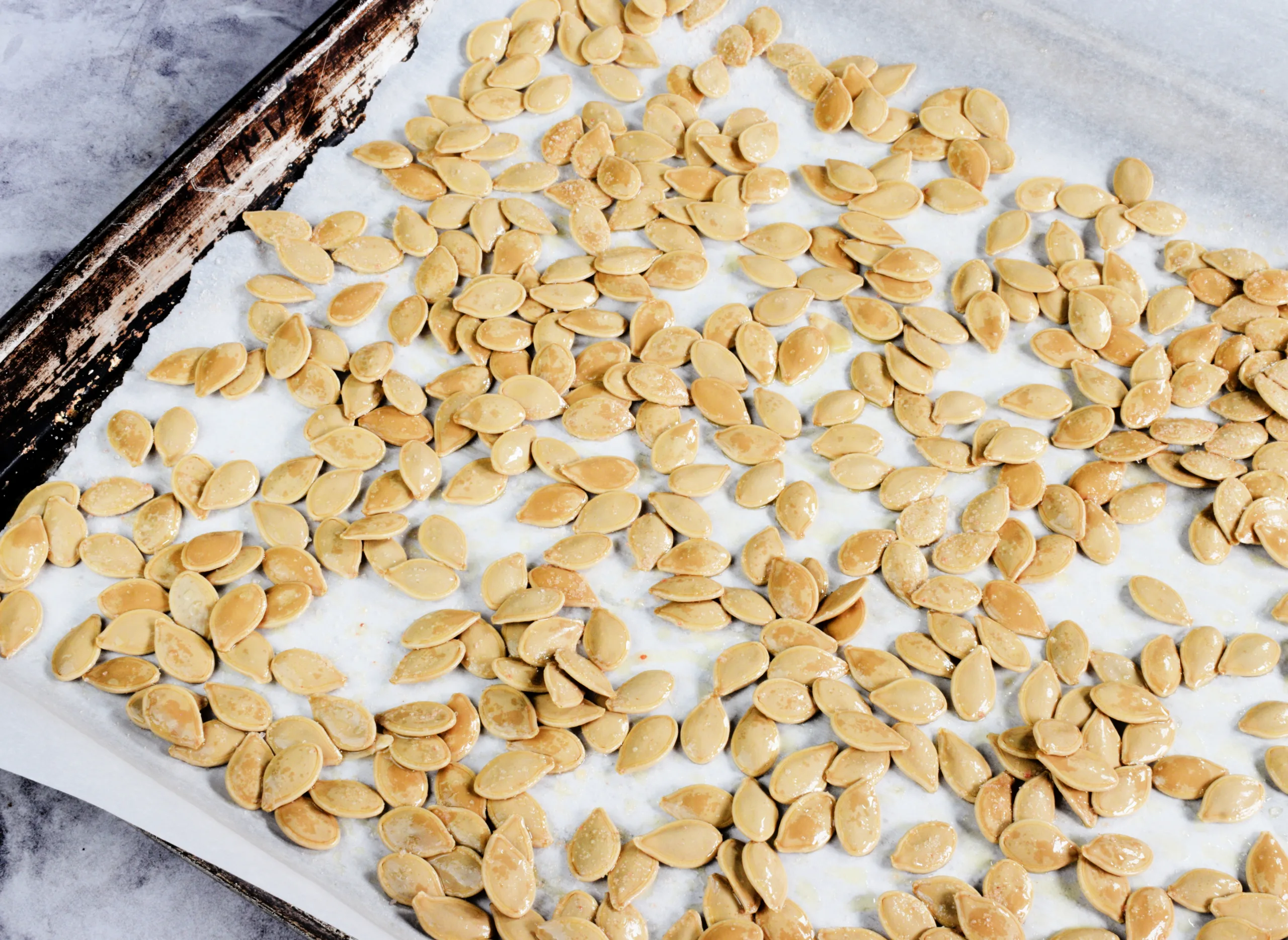 Pumpkin seeds on a cookie sheet for Pumpkin being cut for The Perfect Recipe for How to Roast Pumpkin Seeds.