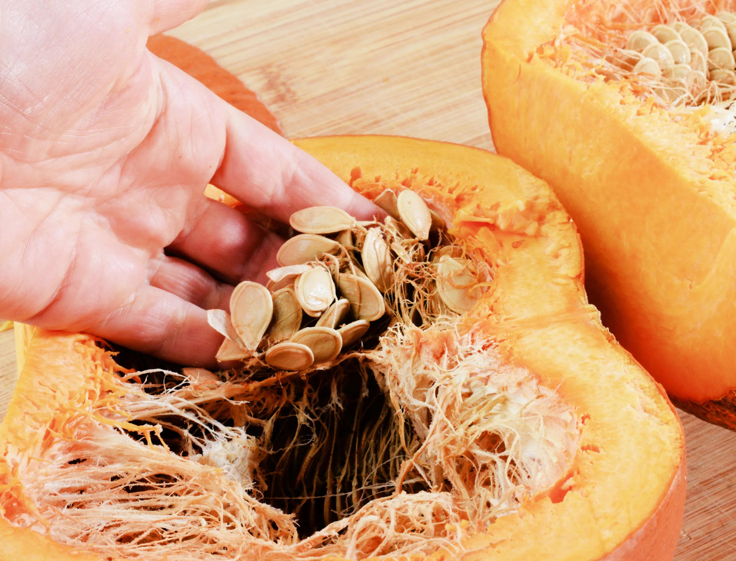 Hand removing pumpkin seeds and stringy pulp from a freshly cut pumpkin.