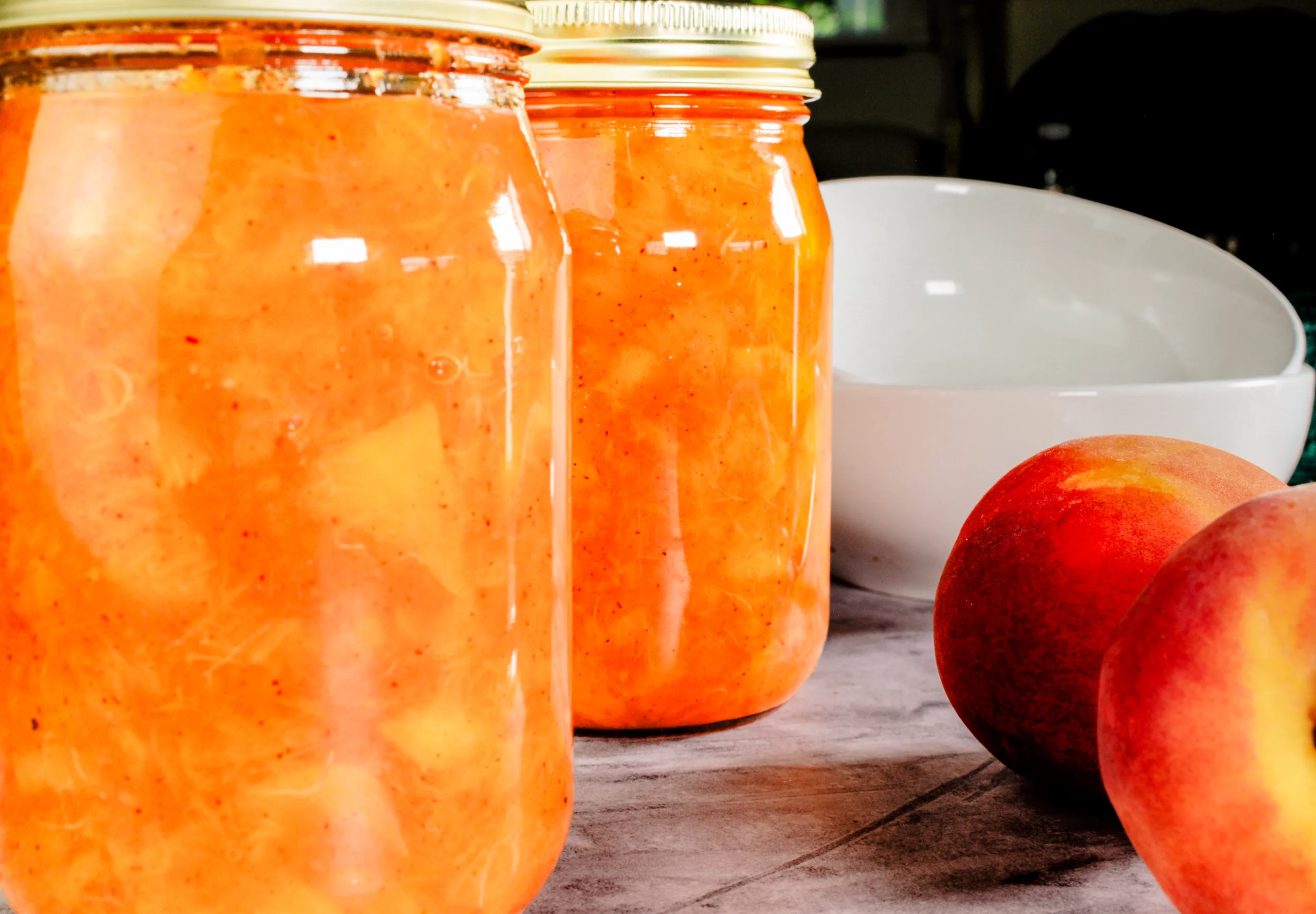 Chunky peach jam dripping from a spoon over an open jar.