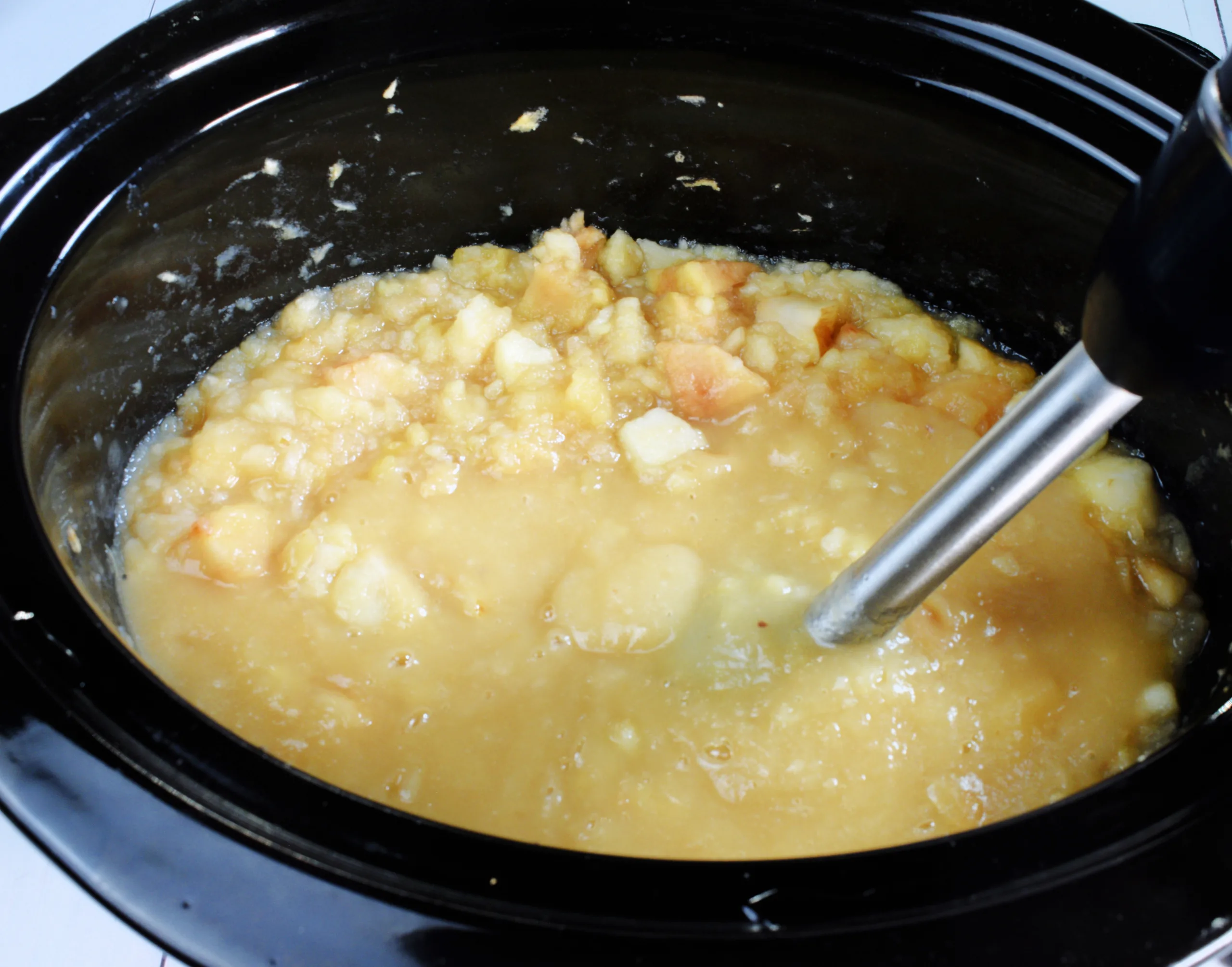 Soft cooked apples being blended in a slow cooker for apple butter.