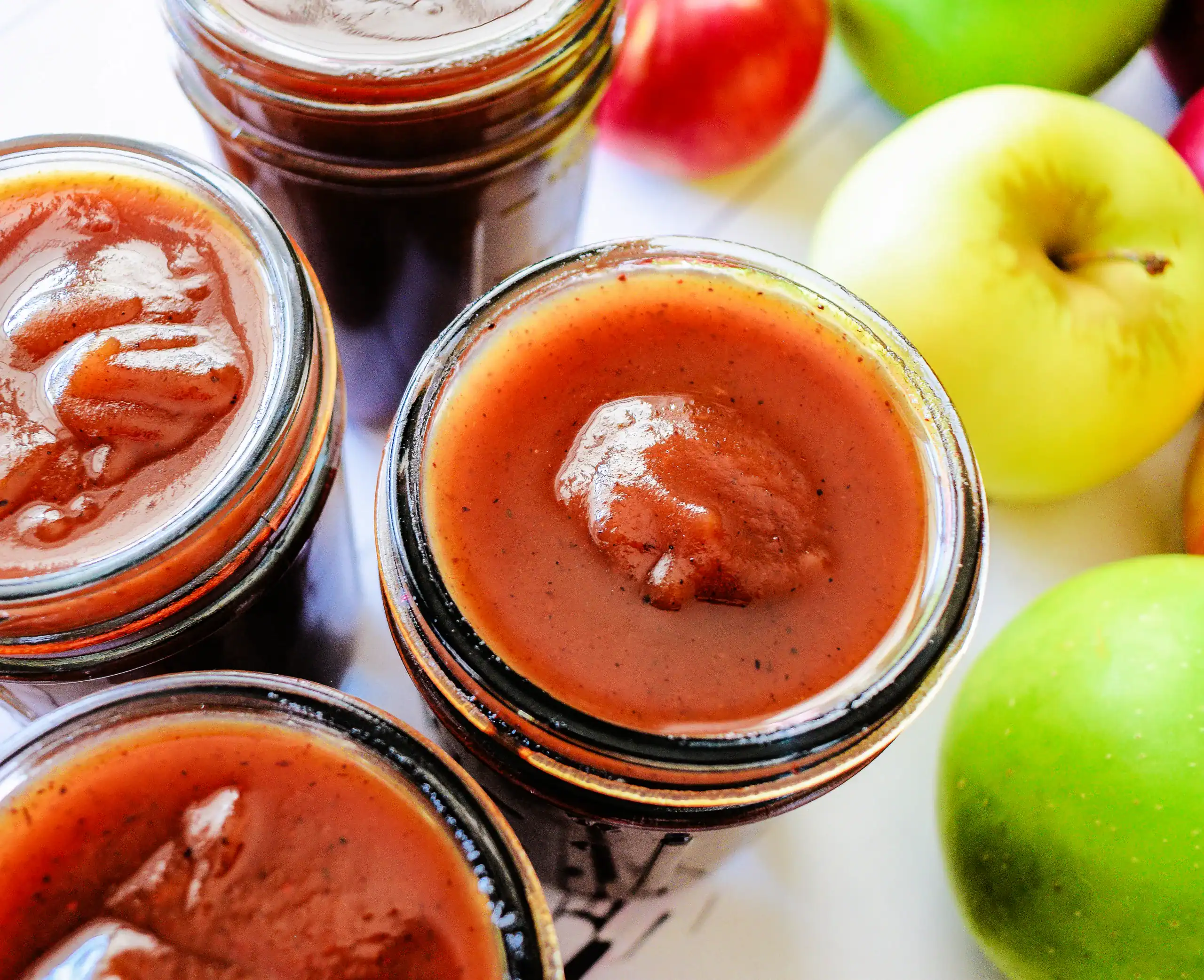 Close-up of thick old fashioned apple butter in jars with apples nearby.