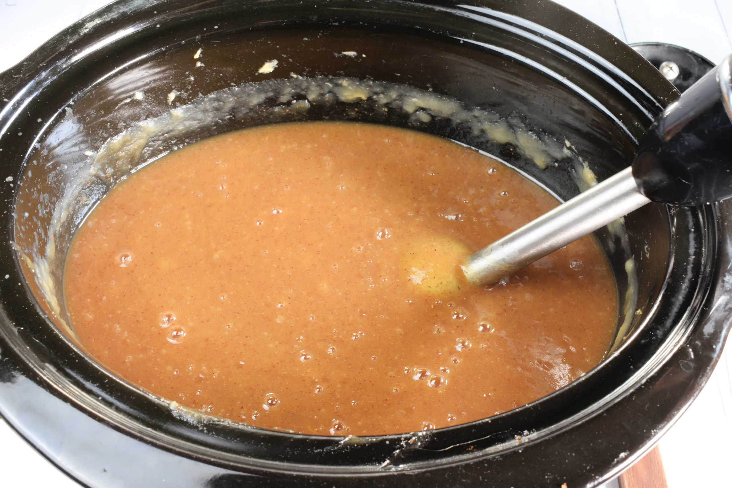 Apple butter being blended smooth in a slow cooker with an immersion blender.