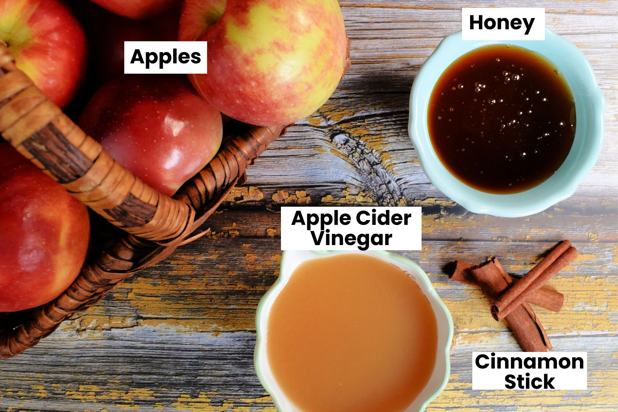 Apple cinnamon shrub ingredients arranged on a rustic wood surface, including fresh apples, honey, apple cider vinegar, and cinnamon sticks.