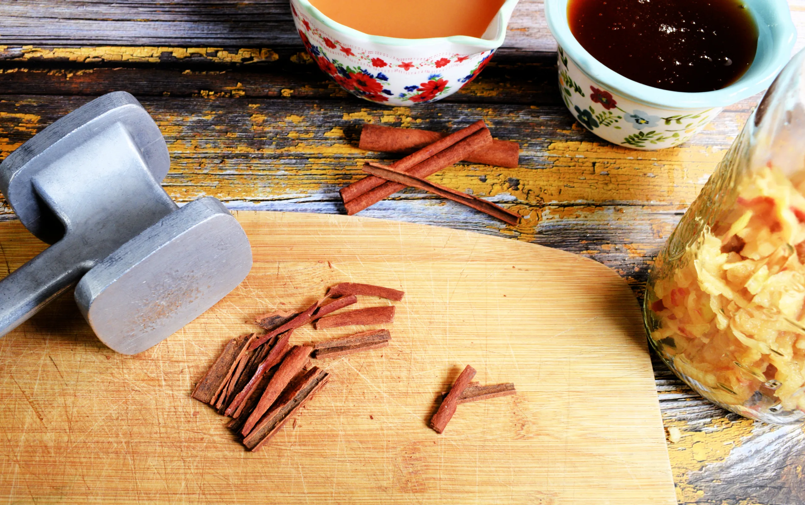Crushed cinnamon sticks on a cutting board with apple cider vinegar, honey, and a mason jar of shredded apples nearby.
