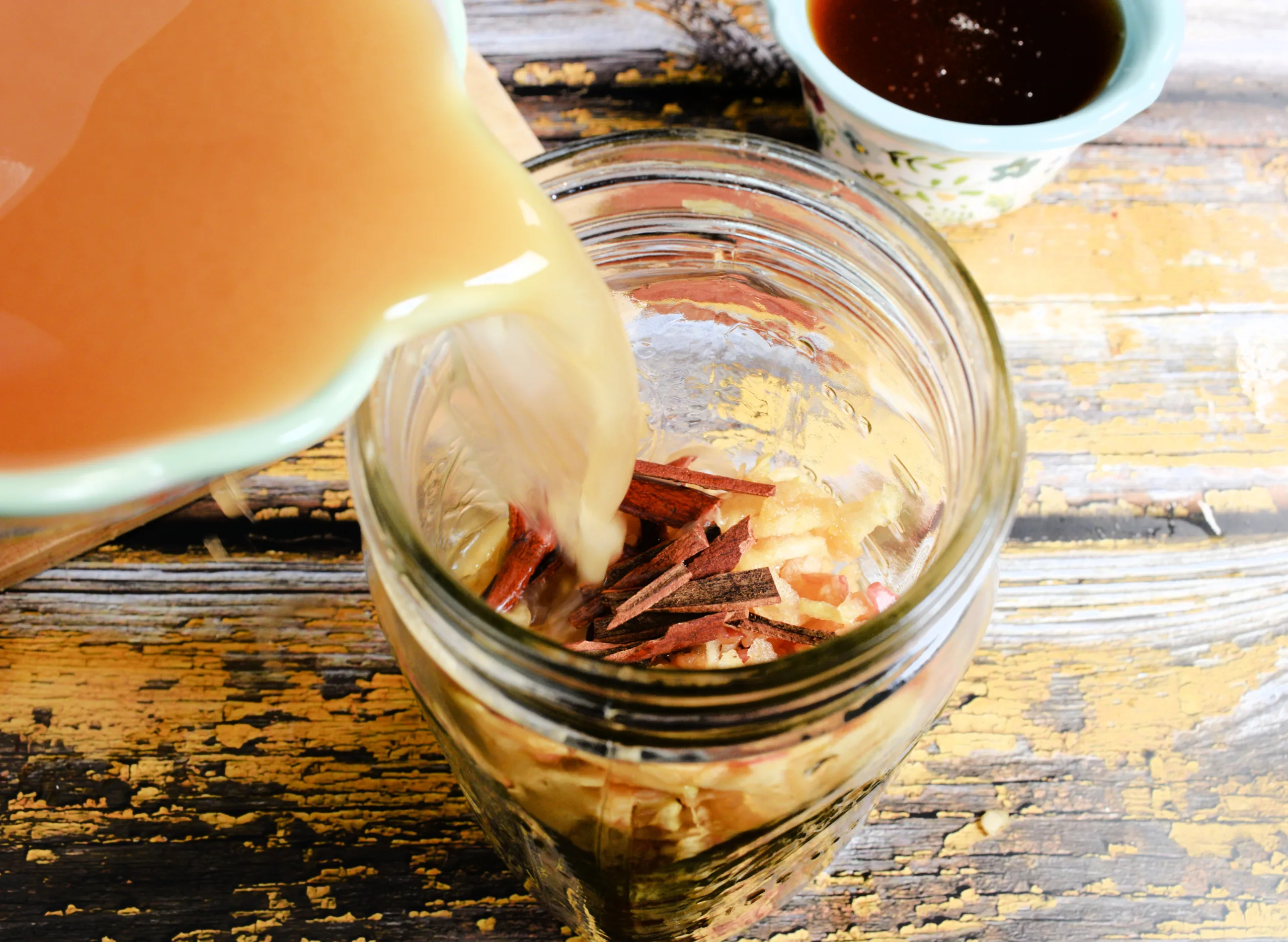 Apple cider vinegar being poured into a mason jar with shredded apples and cinnamon.