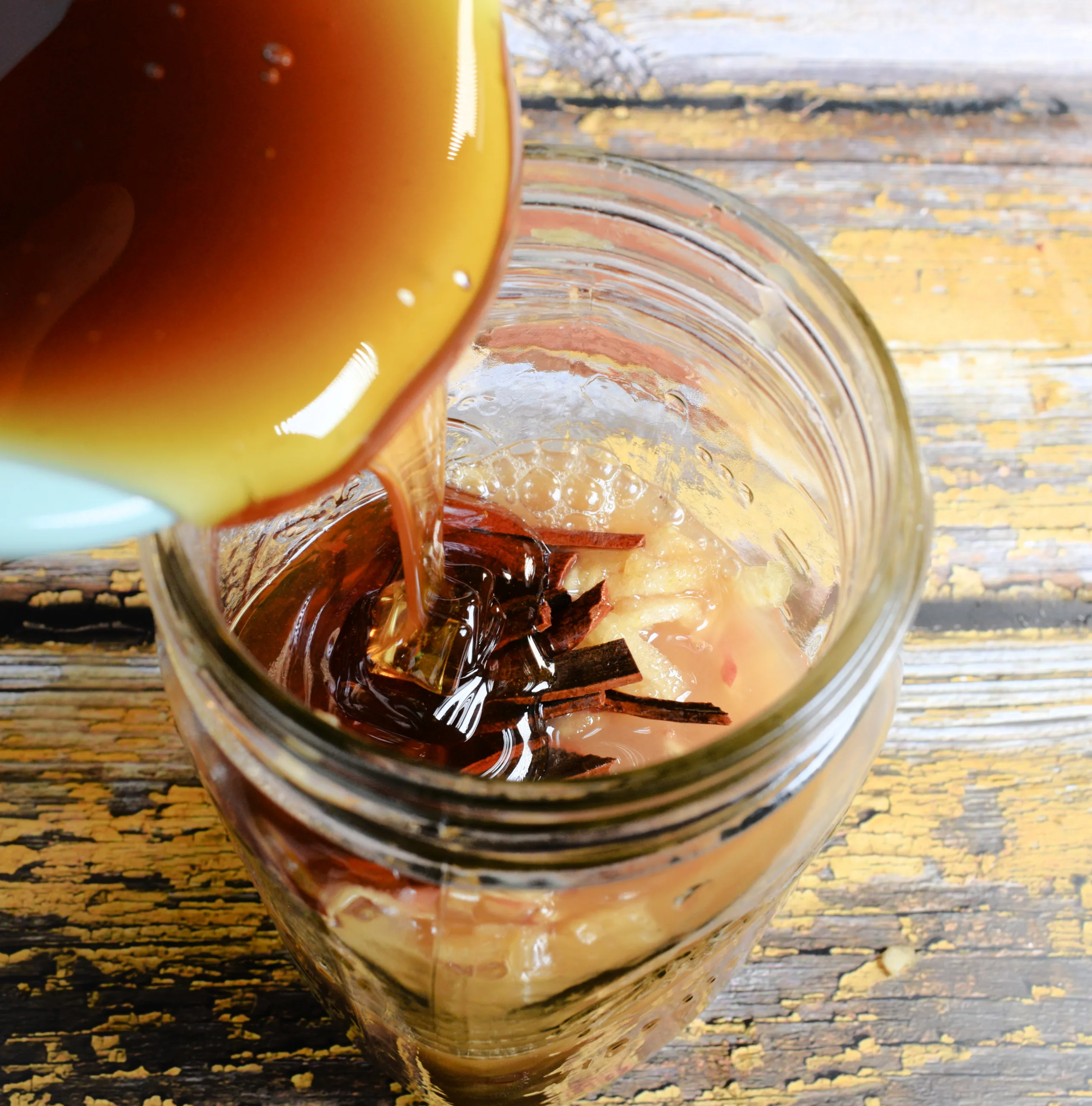 Honey being poured into a mason jar with shredded apples and cinnamon for apple cinnamon shrub.