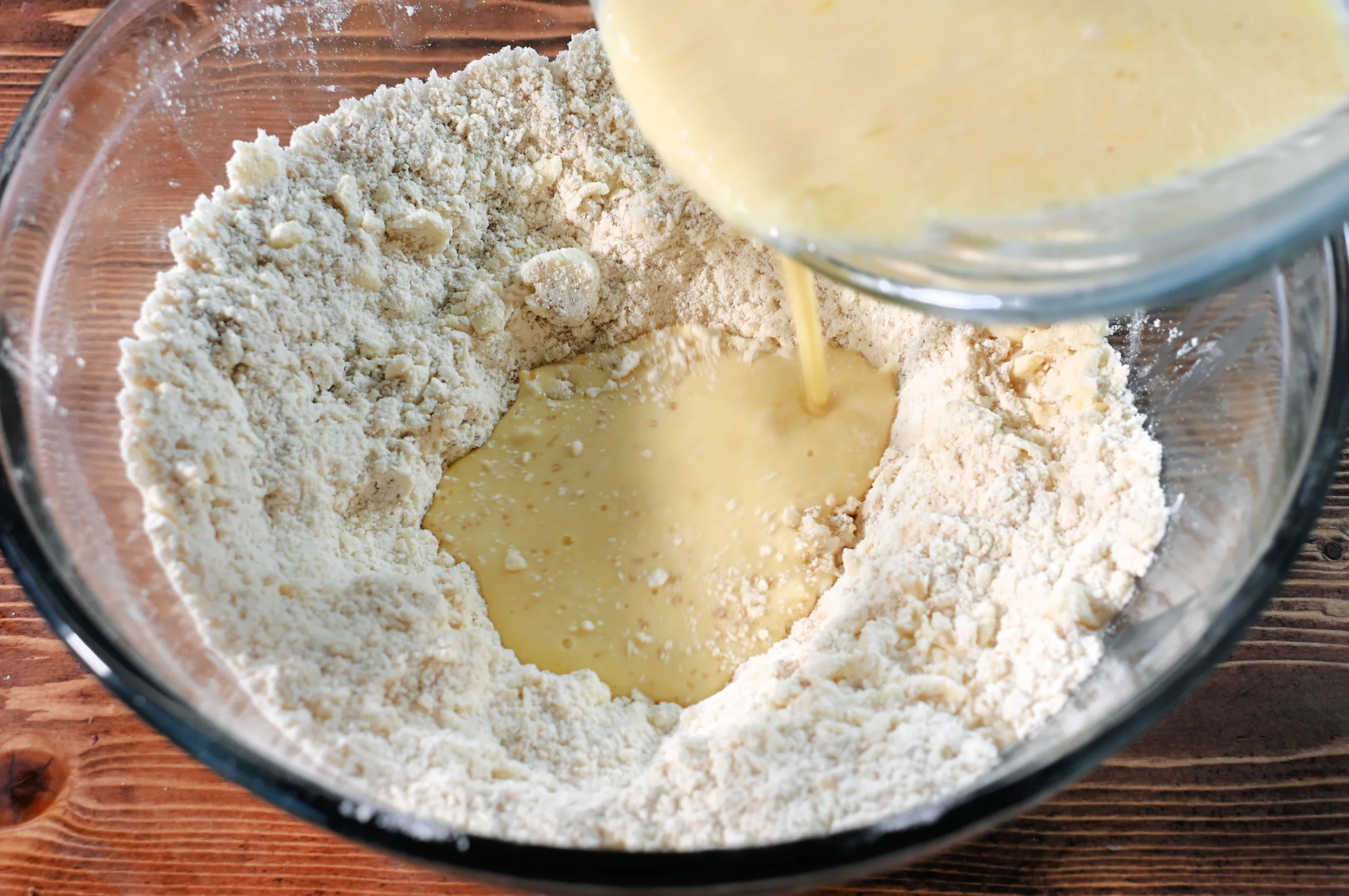 Pouring a creamy mixture of milk and sourdough discard into a bowl of dry ingredients for homemade berry scones.