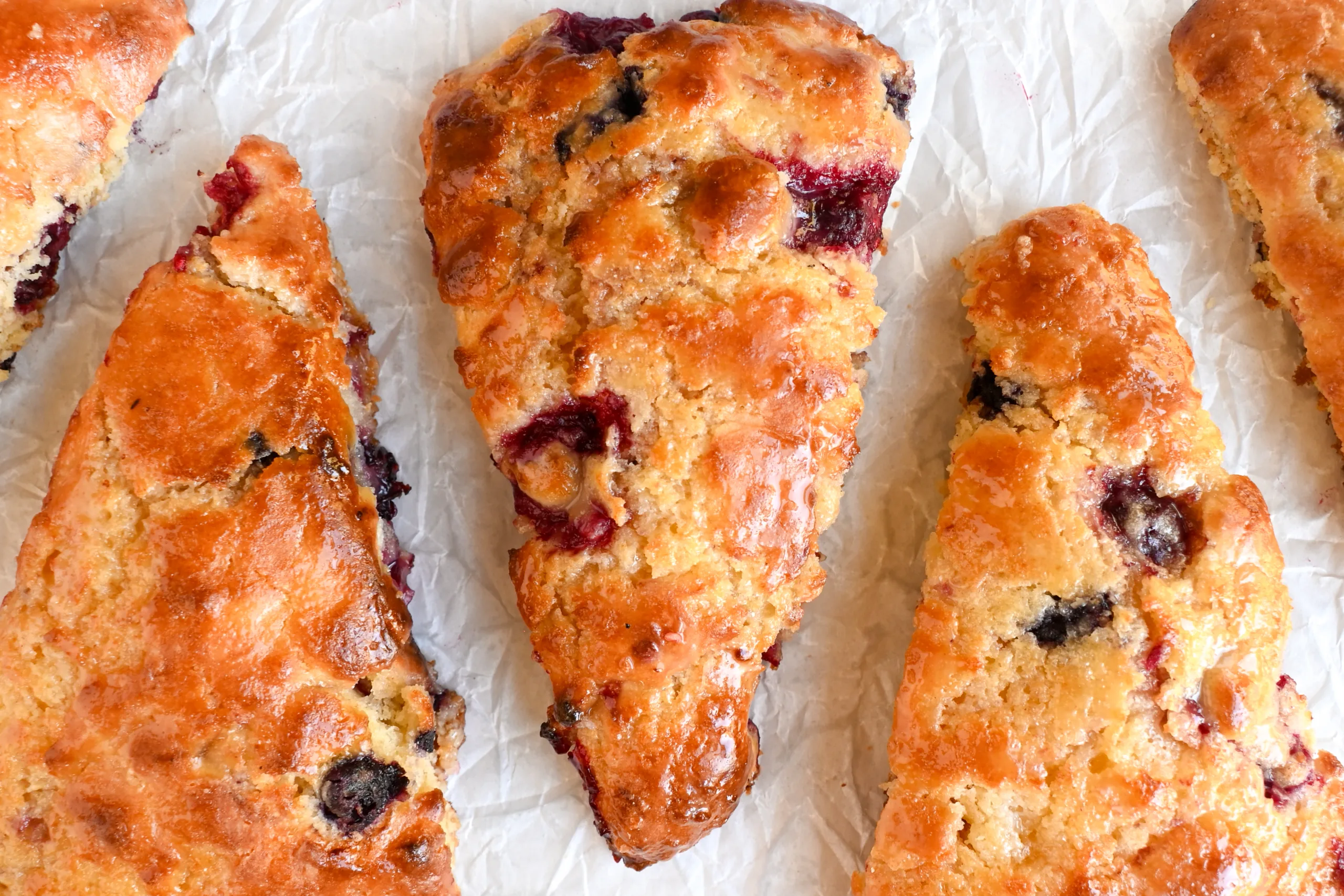 Moist, tender sourdough berry scone with juicy raspberries and blueberries, glistening with honey glaze.