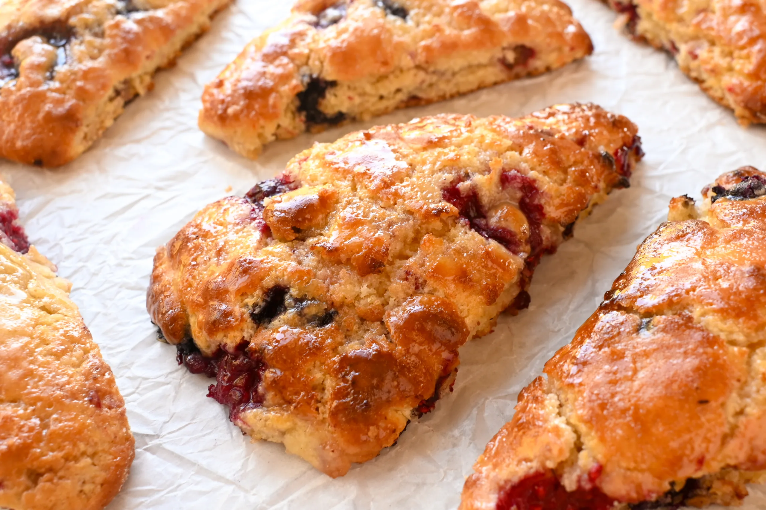 Moist, tender sourdough berry scone with juicy raspberries and blueberries, glistening with honey glaze.