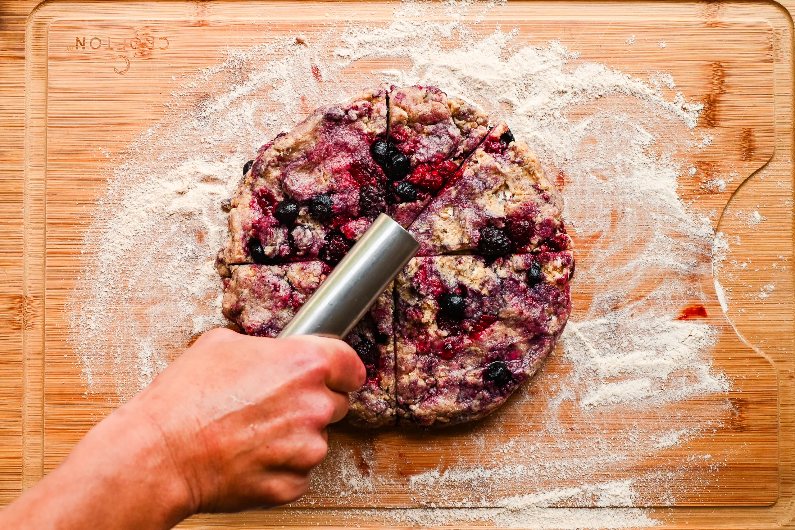 Cutting sourdough berry scone dough into triangle wedges using a bench scraper before baking.