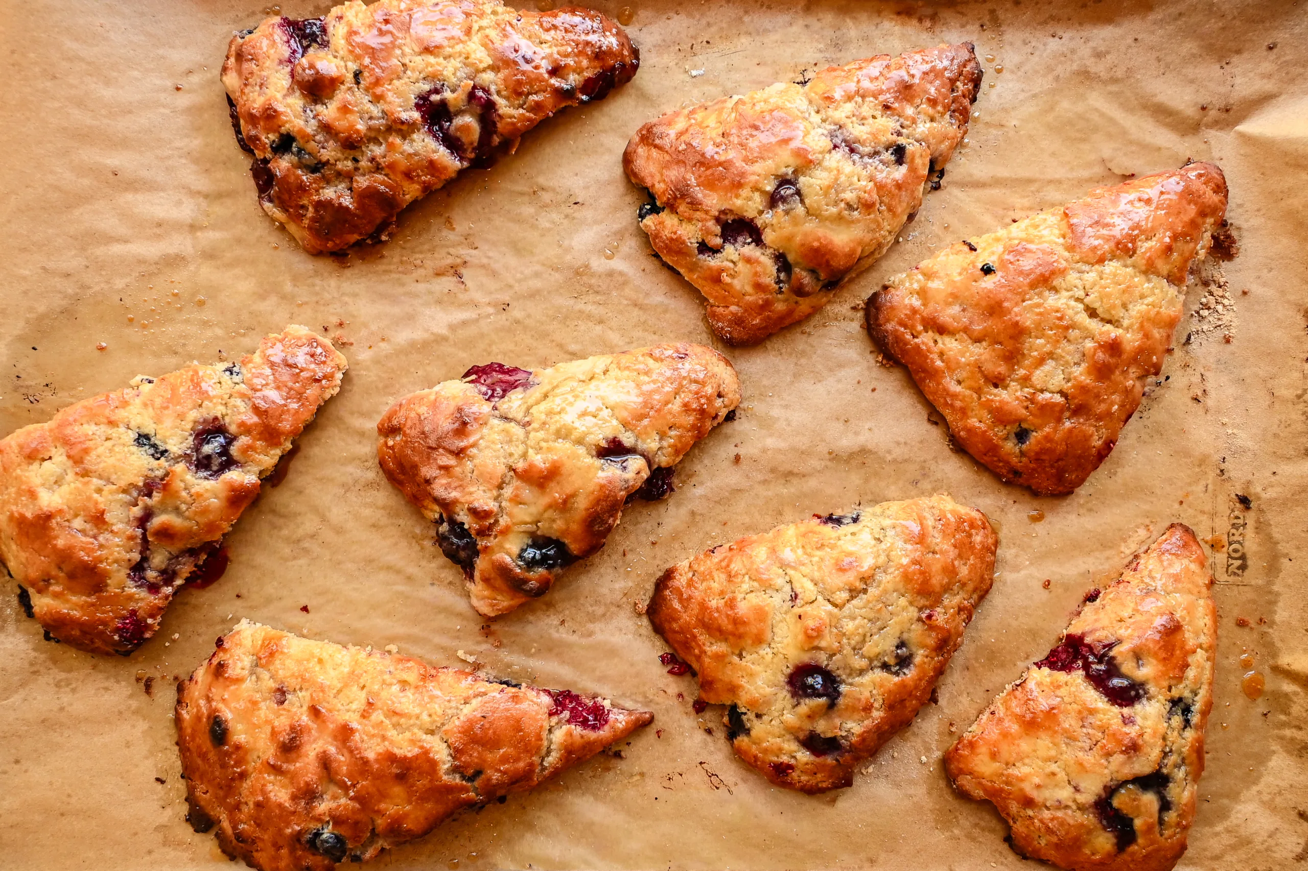 Golden brown sourdough discard berry scones cooling on parchment after baking, showing flaky layers.