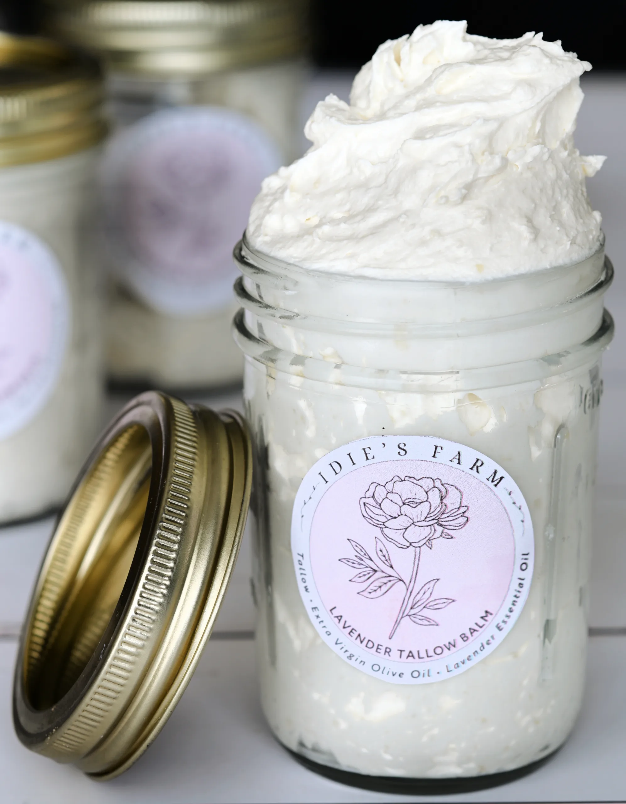 Close-up of homemade lavender whipped tallow balm in a glass jar with a gold lid resting beside it