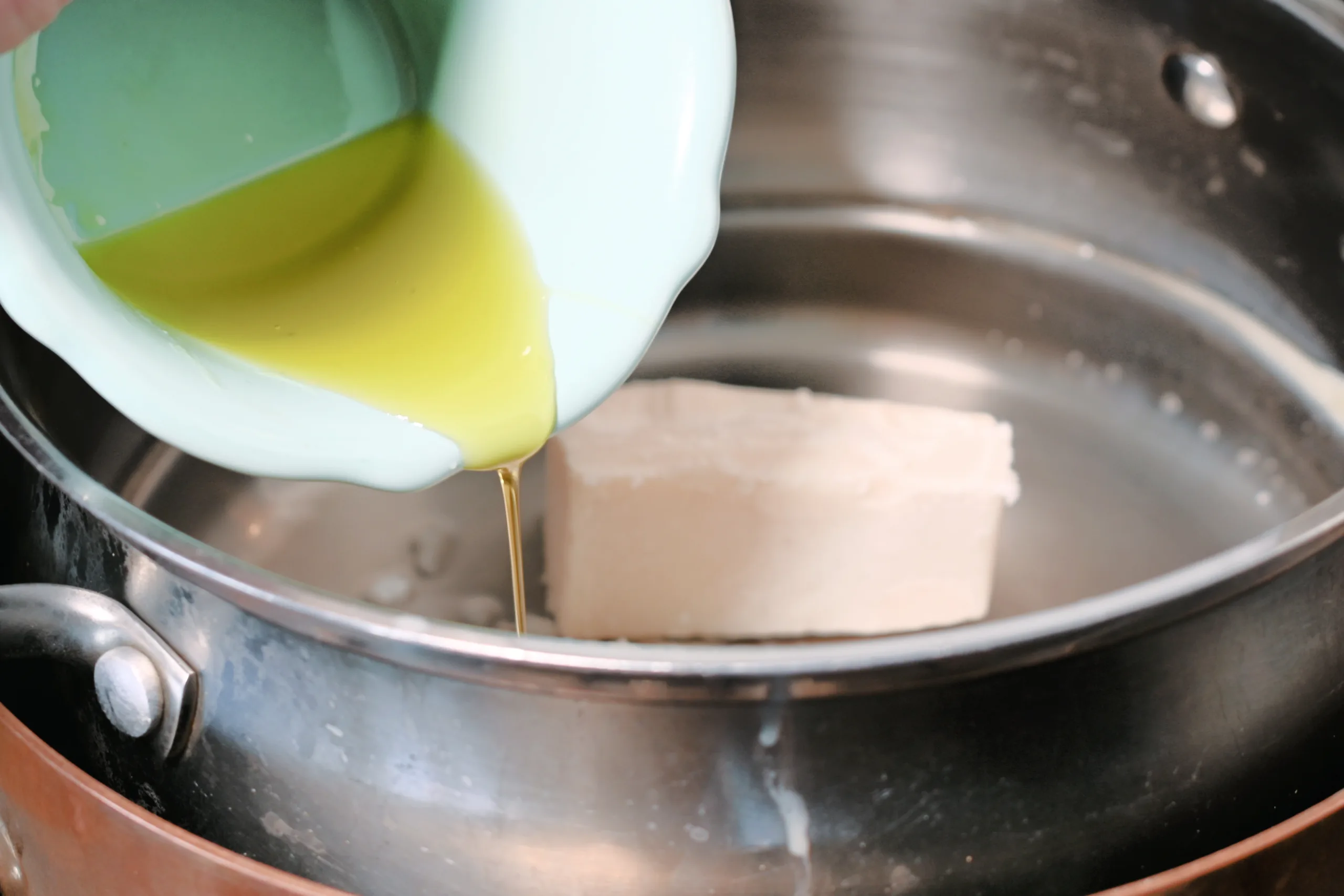 Olive oil being poured into melted beef tallow in a double boiler for homemade whipped tallow balm